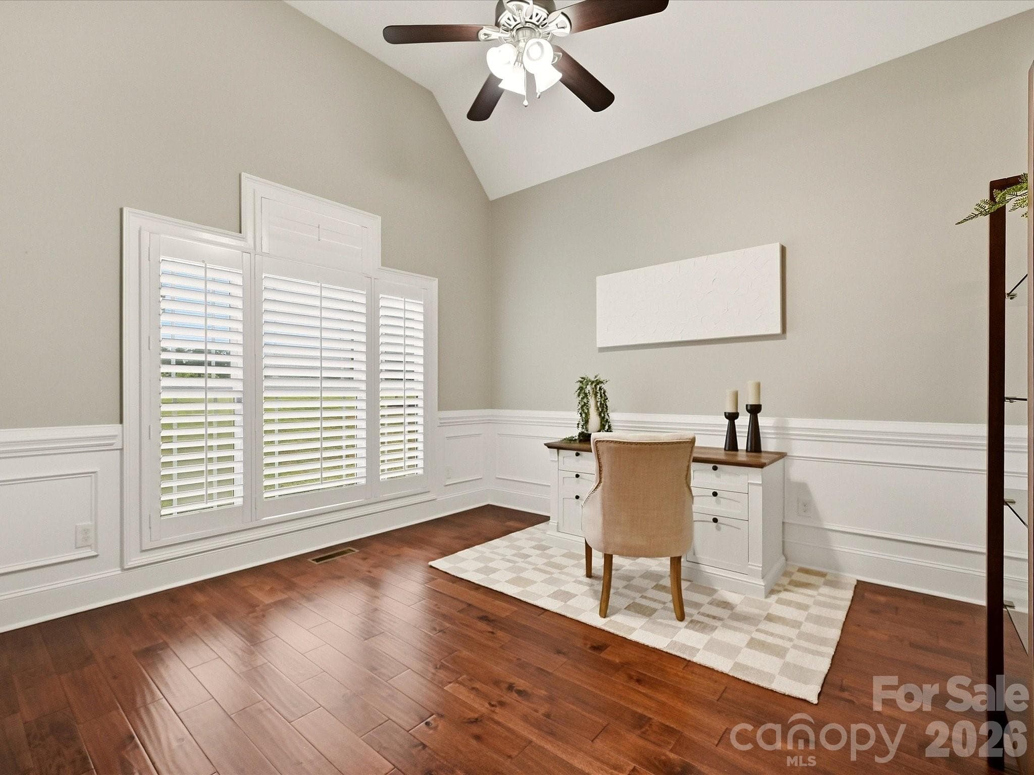 A bright home office features vaulted ceilings, gorgeous flooring, elegant wainscoting, plantation shutters, and generous space for a comfortable work-from-home setup. - 3167 James Plantation Drive, Denver