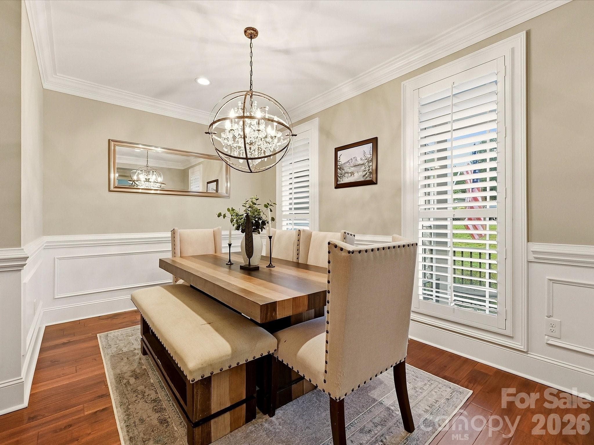 An elegant formal dining room features rich floors, classic wainscoting and crown molding, plantation shutters, and a striking statement chandelier. - 3167 James Plantation Drive, Denver