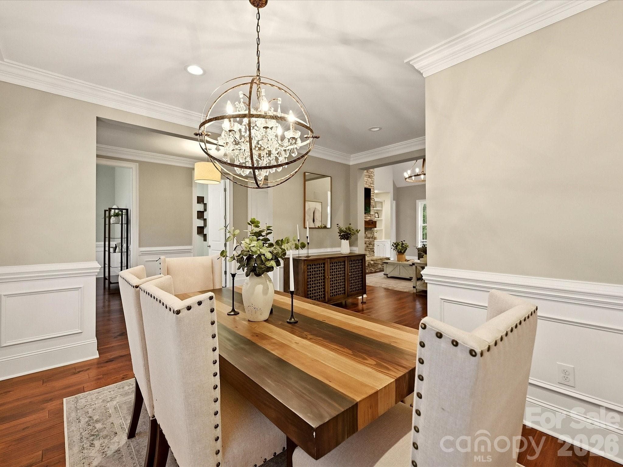 An elegant formal dining room features rich flooring, classic wainscoting and crown molding, plantation shutters, and a striking statement chandelier. - 3167 James Plantation Drive, Denver