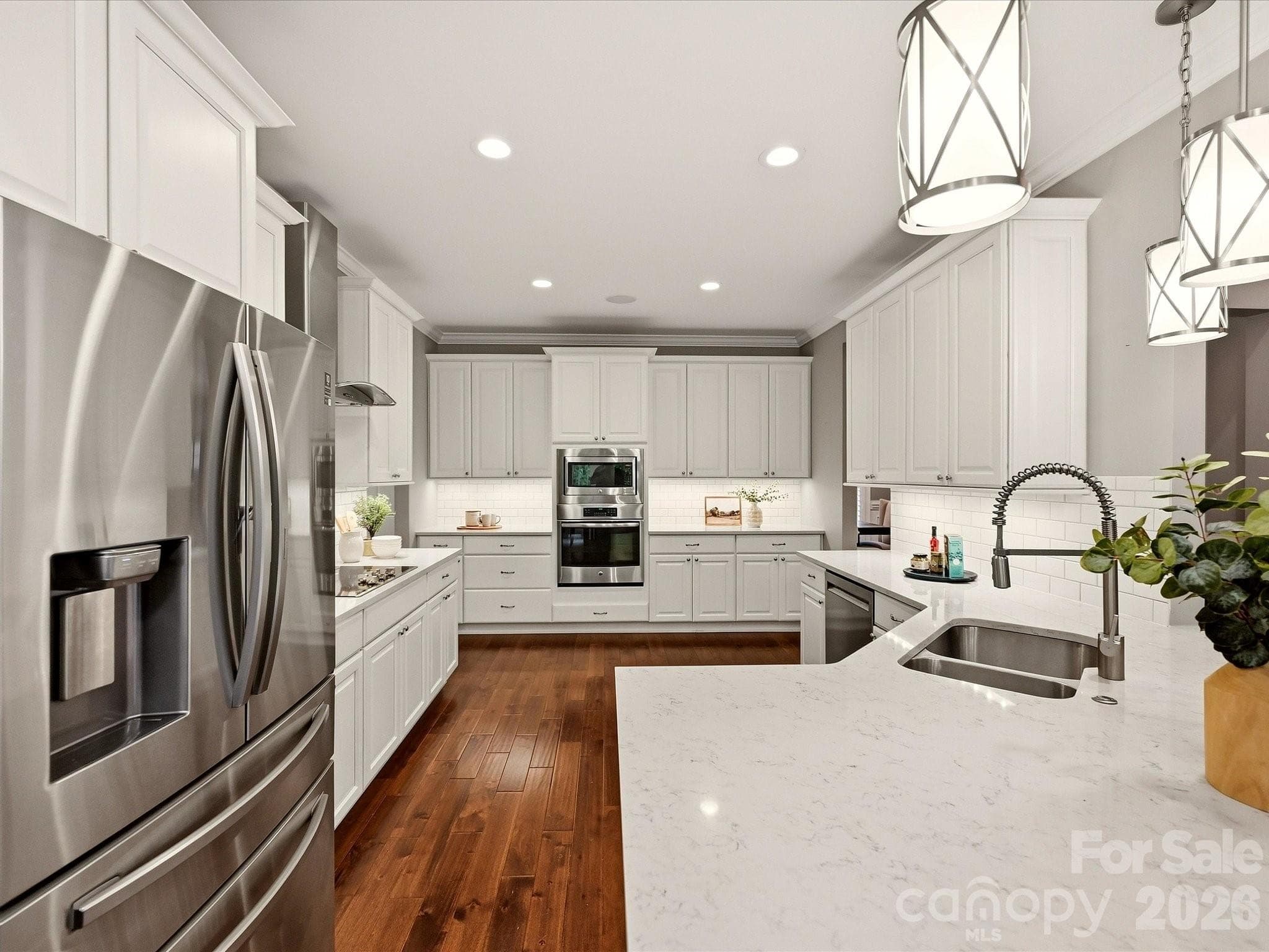 A beautifully updated kitchen features crisp white cabinetry, quartz countertops, stainless steel appliances, subway tile backsplash, stylish pendant lighting, and an expansive island with generous workspace and seating. - 3167 James Plantation Drive, Denver