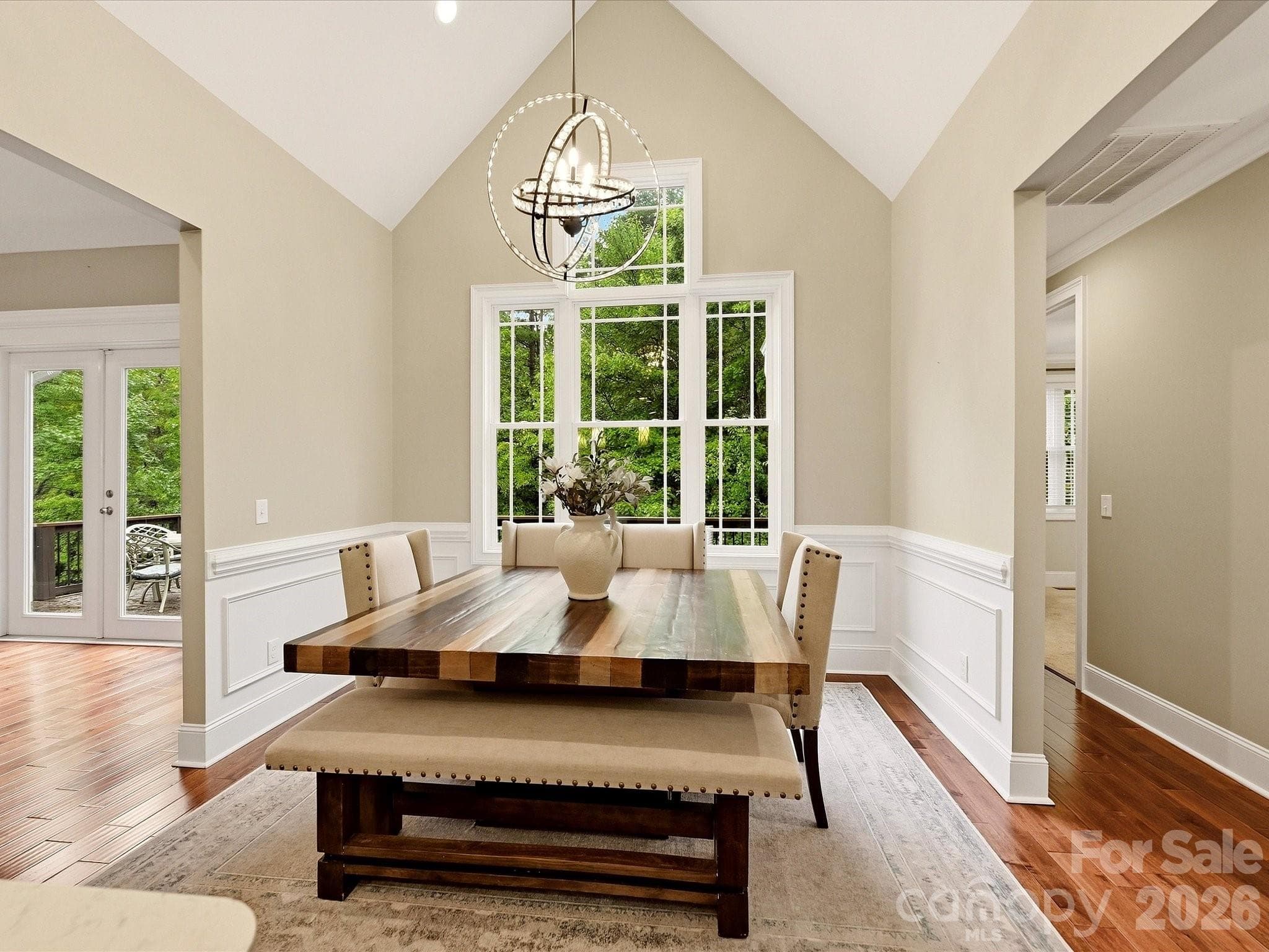 A light-filled breakfast/dining area features vaulted ceilings, hardwood floors, elegant wainscoting, a statement chandelier, and expansive windows overlooking the surrounding greenery. - 3167 James Plantation Drive, Denver