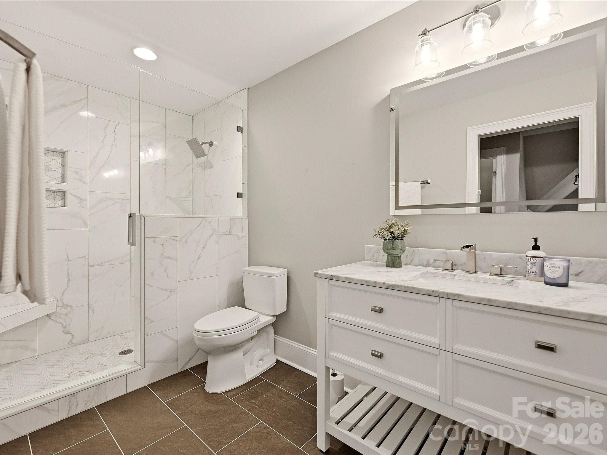 A beautifully updated full bath features a spacious marble-look tiled shower with glass enclosure, modern vanity with stone countertop, contemporary fixtures, and stylish tile flooring. - 3167 James Plantation Drive, Denver