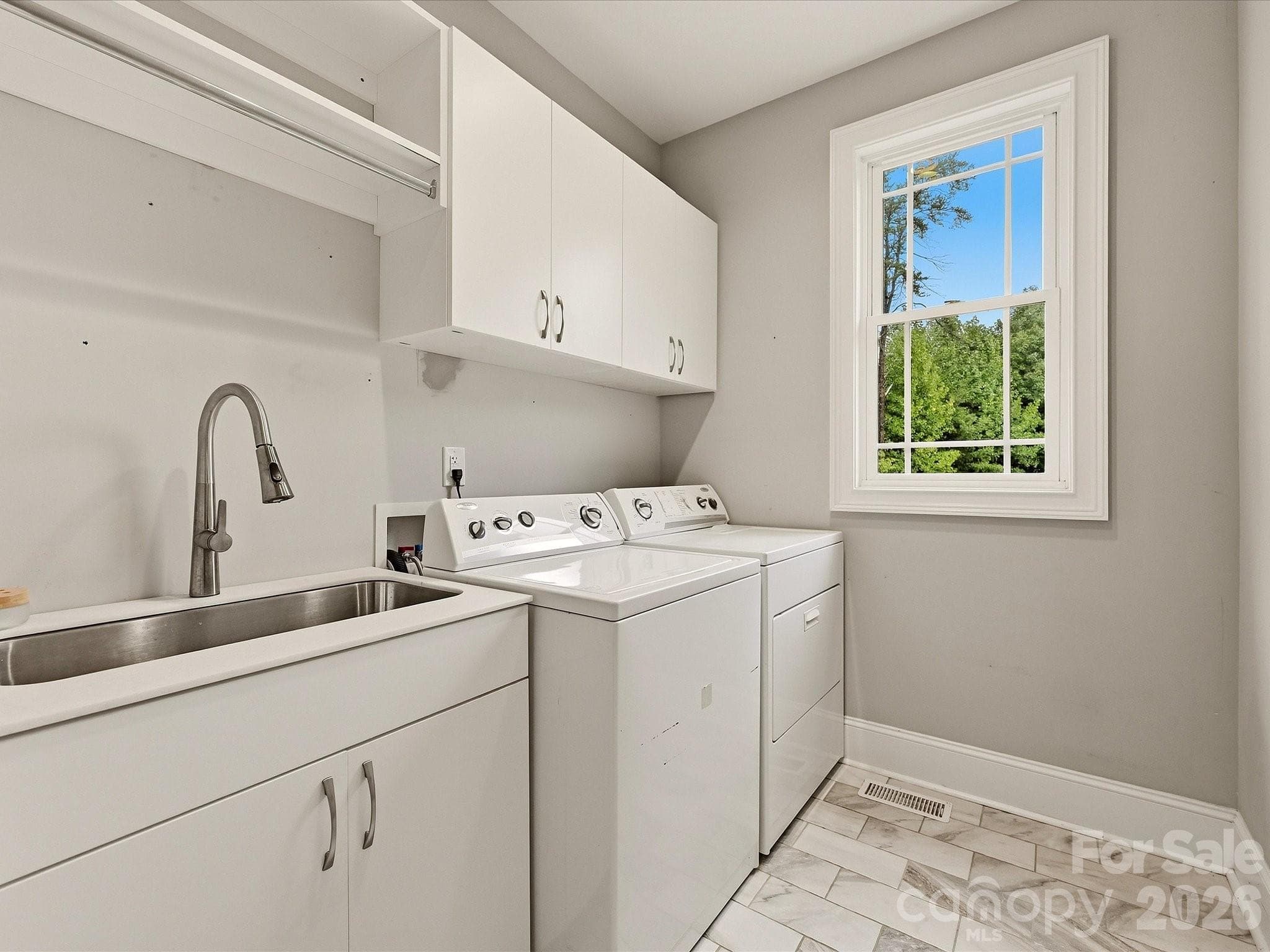 A bright laundry room offers a utility sink, built-in cabinetry, hanging space, tile flooring, and a window providing natural light. - 3167 James Plantation Drive, Denver