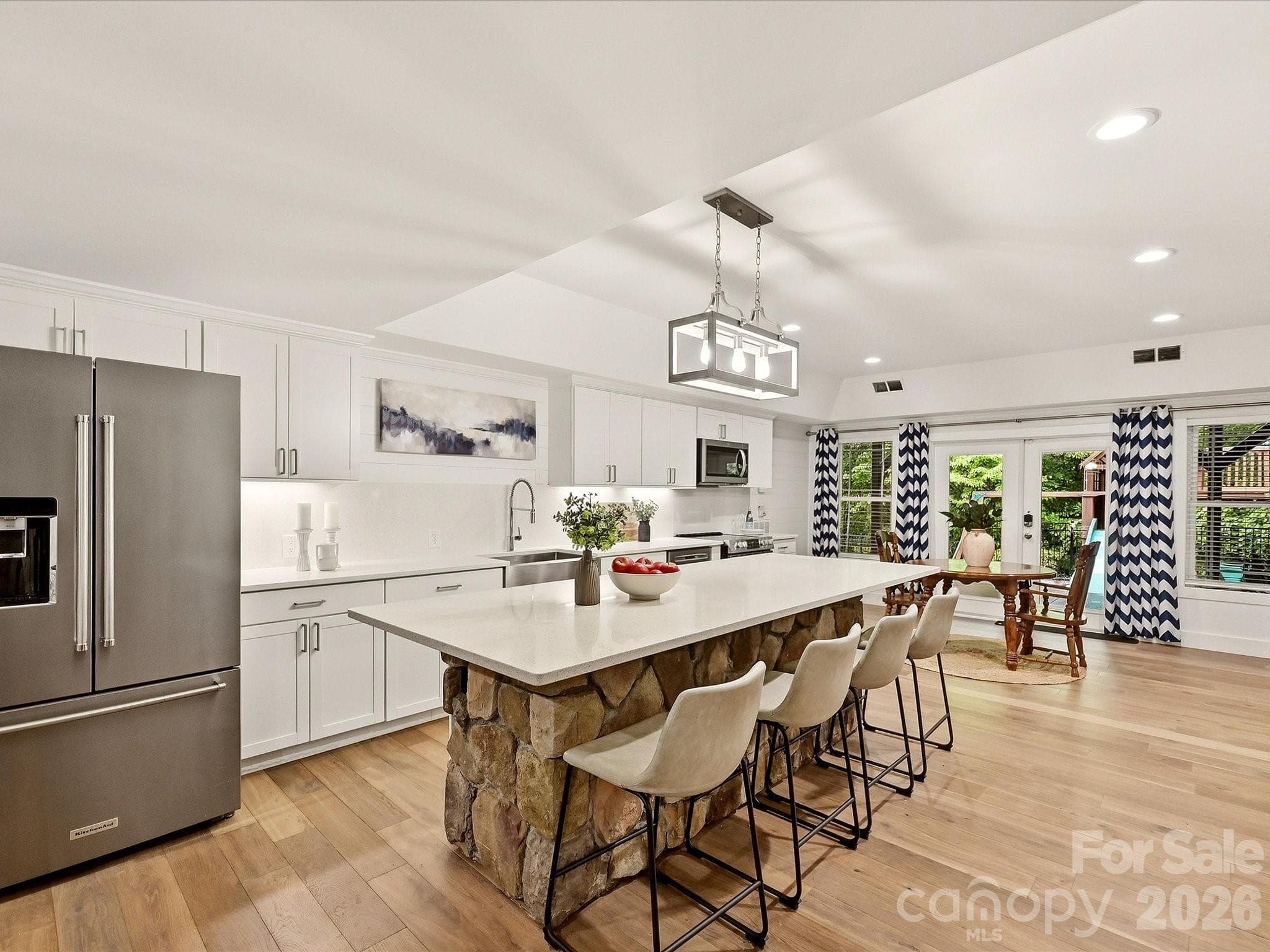 The basement level kitchen features crisp white cabinetry, quartz countertops, stainless steel appliances, a spacious stone-accented island with seating, and an open layout ideal for entertaining. - 3167 James Plantation Drive, Denver