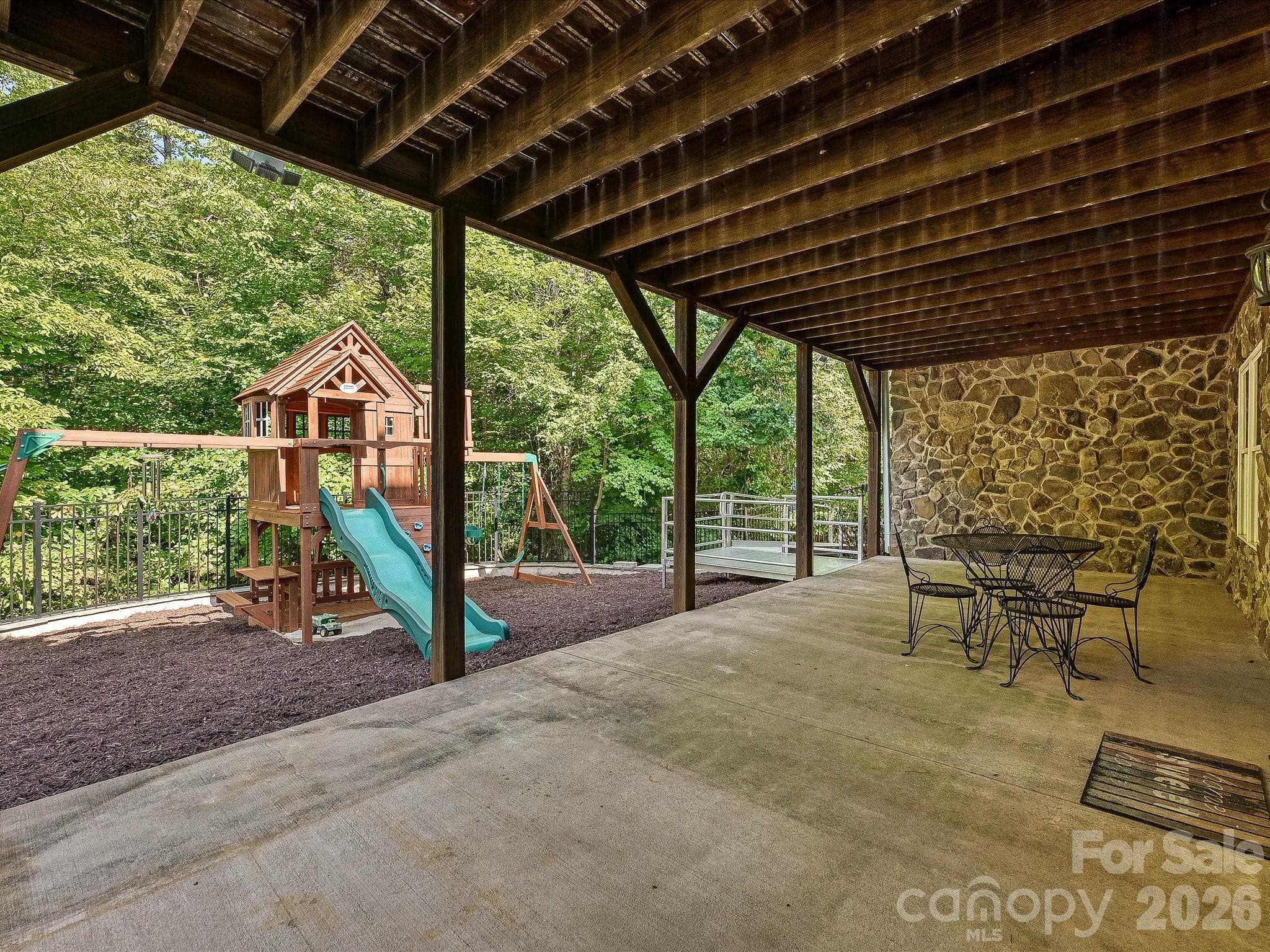 A spacious covered patio with exposed wood beams and stone accents provides a shaded outdoor retreat overlooking the fenced, tree-lined backyard and play area. - 3167 James Plantation Drive, Denver
