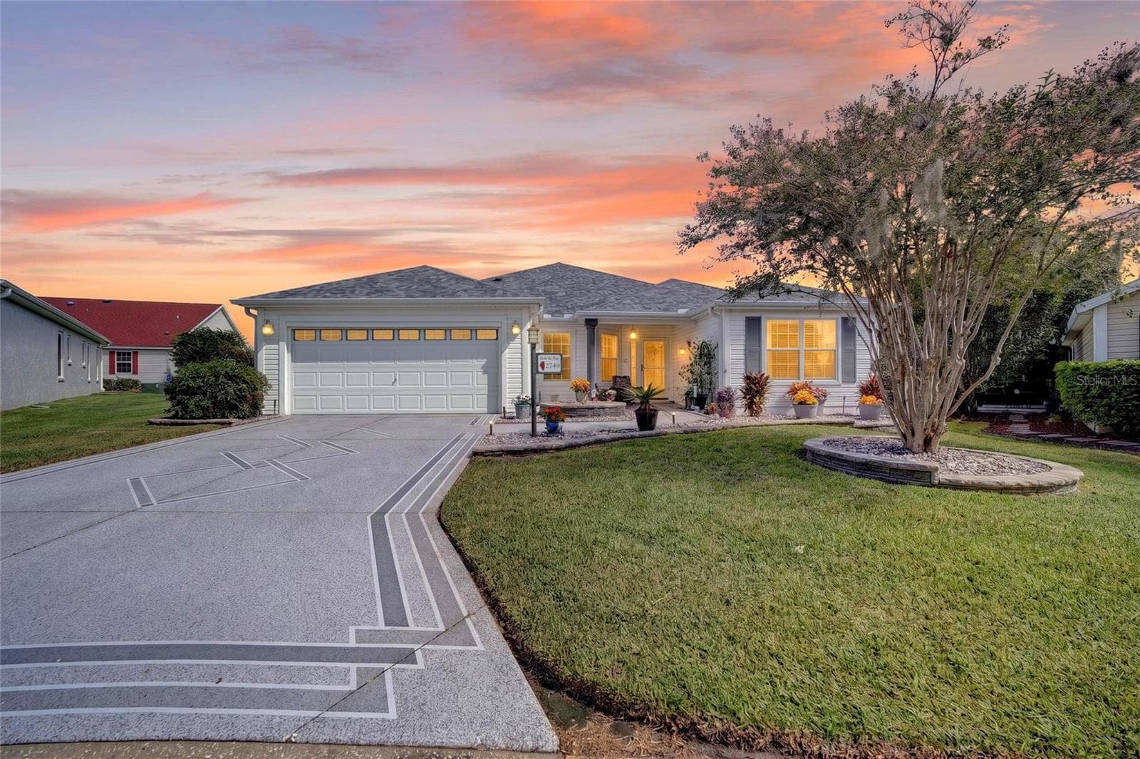 Front Exterior at Twilight: Evening exterior view highlights the home's welcoming covered entry, illuminated windows, attached garage, and landscaped front yard. - 2749 BANYAN PL, THE VILLAGES