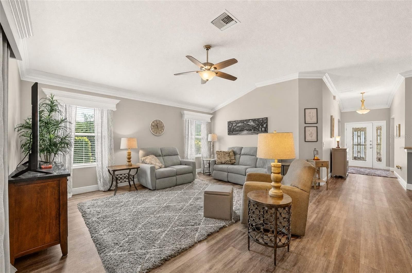 Living Room: Another view highlights the open, comfortable living space with multiple windows, neutral finishes, crown molding, and easy flow to the entry and adjoining areas. - 2749 BANYAN PL, THE VILLAGES