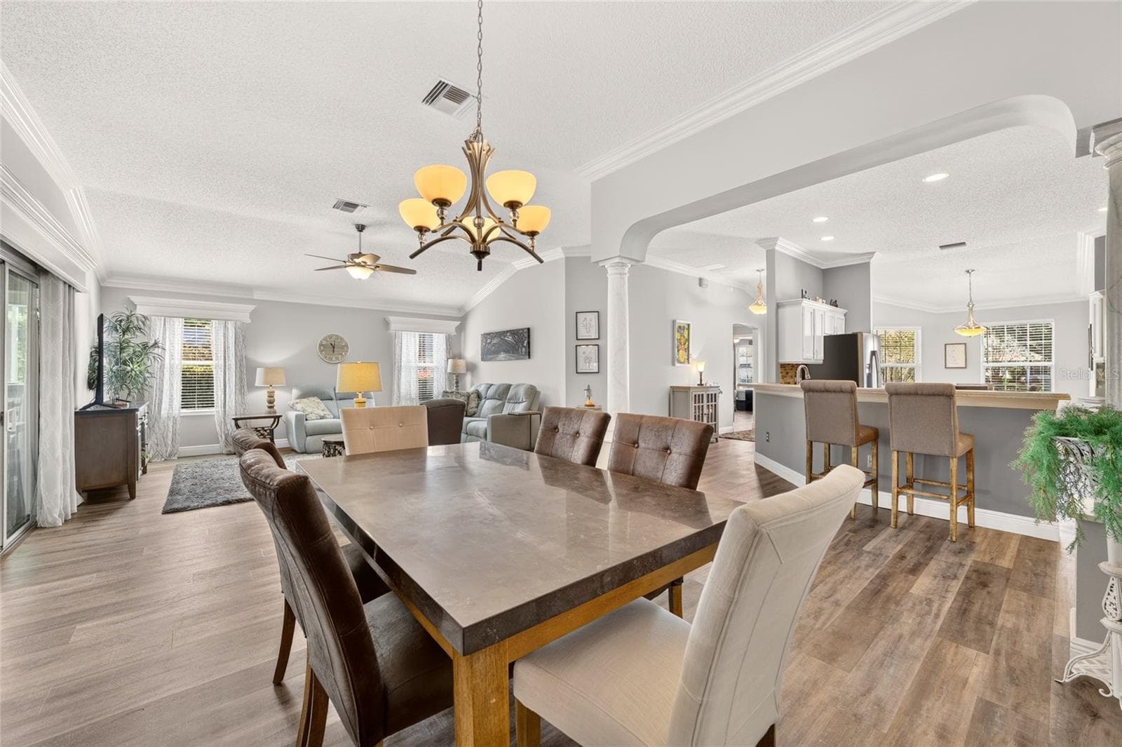 Dining Area: Open dining space connects naturally with the living room and kitchen, complemented by crown molding, a statement chandelier, and continuous wood-look flooring. - 2749 BANYAN PL, THE VILLAGES