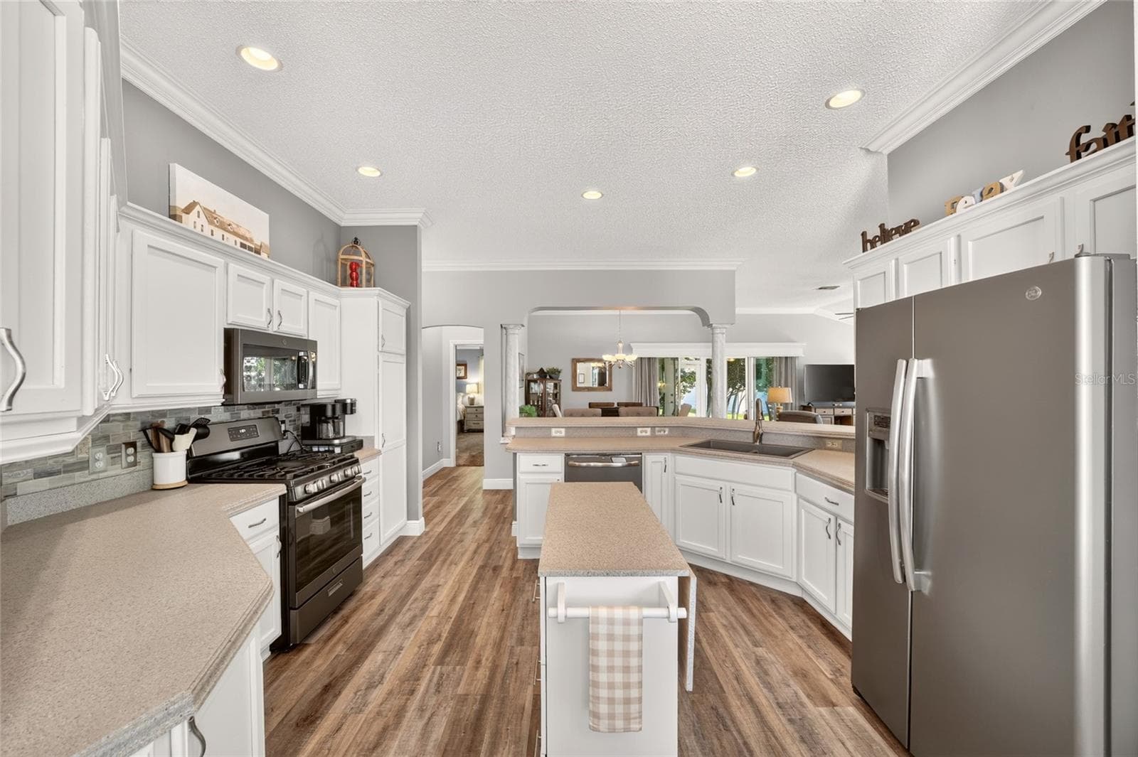 Kitchen: Generously sized kitchen features white cabinetry, ample counter space, recessed lighting, stainless-finish appliances, a center work island, and an open pass-through to the main living area. - 2749 BANYAN PL, THE VILLAGES