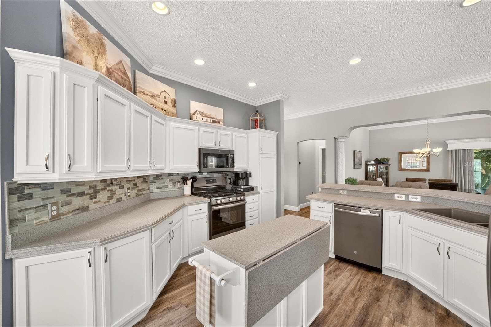 Kitchen: Additional kitchen view showcases extensive cabinetry, a tile backsplash, broad work surfaces, center island, and an open layout overlooking the dining area. - 2749 BANYAN PL, THE VILLAGES