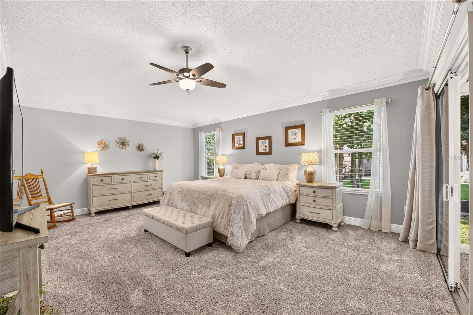 Primary Bedroom: Spacious bedroom features soft carpeting, crown molding, a ceiling fan, multiple windows, and direct access to the outdoor living area. - 2749 BANYAN PL, THE VILLAGES