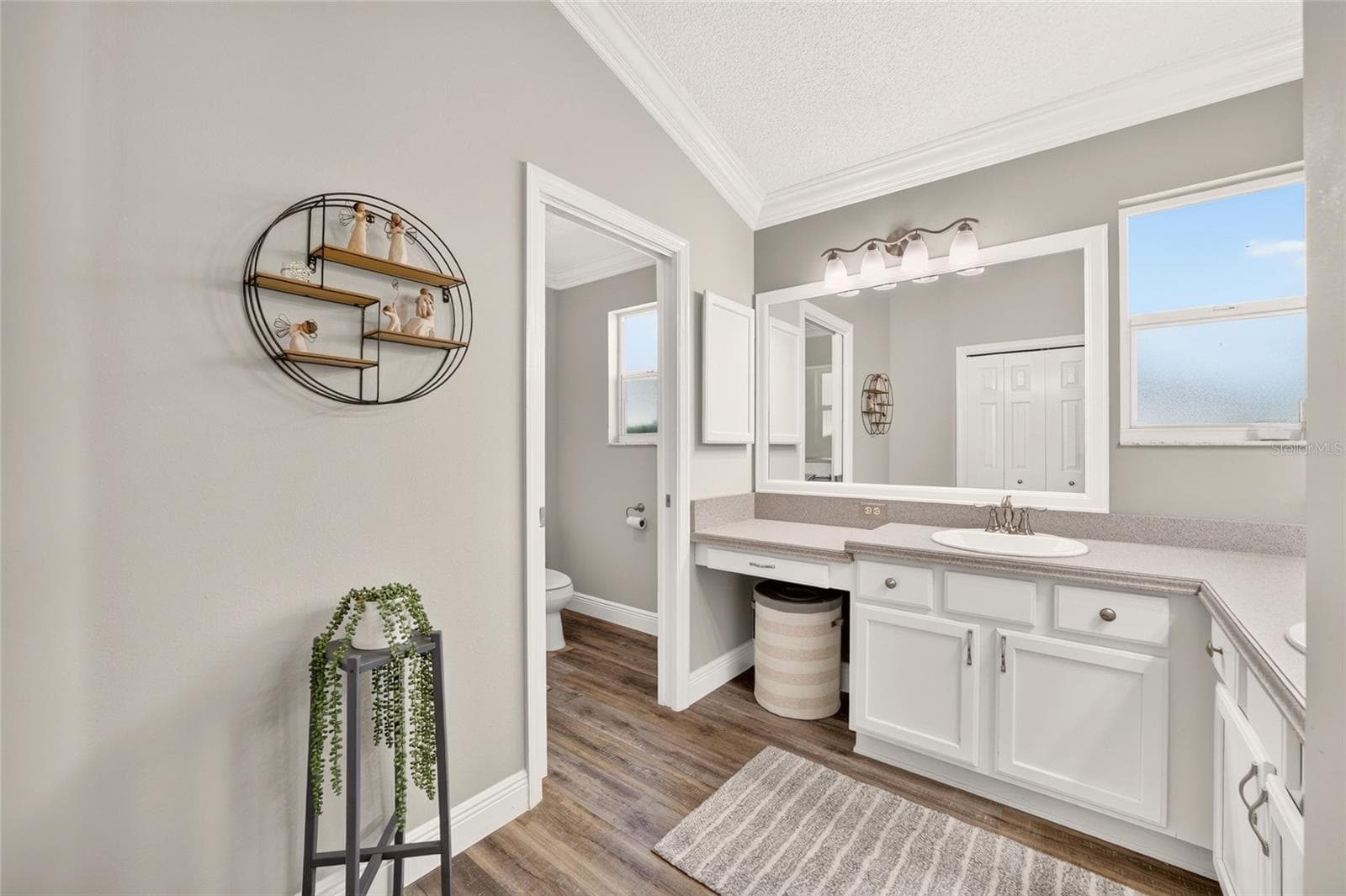 Primary Bathroom: Spacious vanity area features abundant white cabinetry, generous counter space, a large wall mirror, crown molding, and natural light. - 2749 BANYAN PL, THE VILLAGES