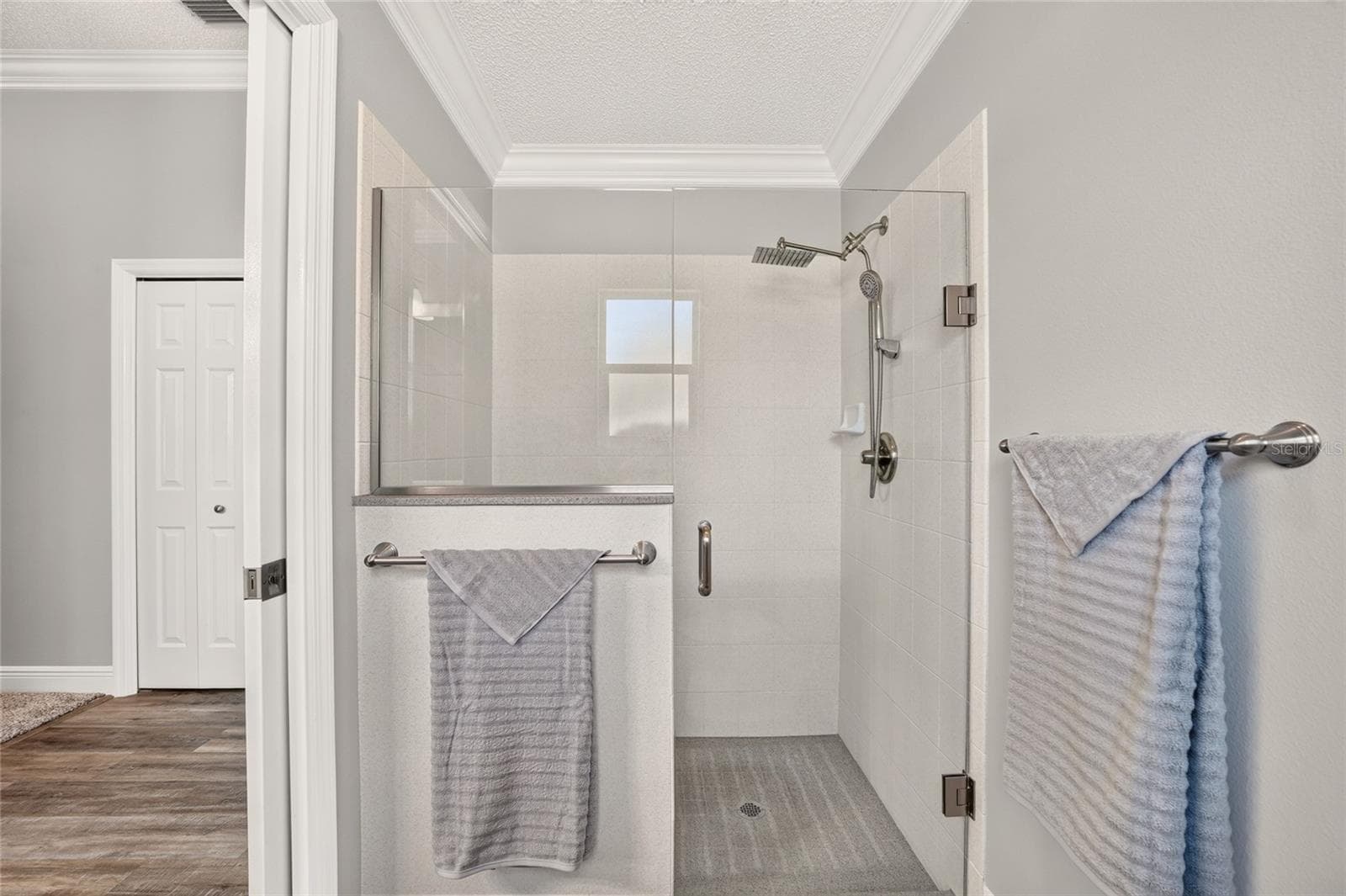 Primary Shower: Walk-in tiled shower features a frameless glass enclosure, multiple showerheads, and a low-threshold entry. - 2749 BANYAN PL, THE VILLAGES