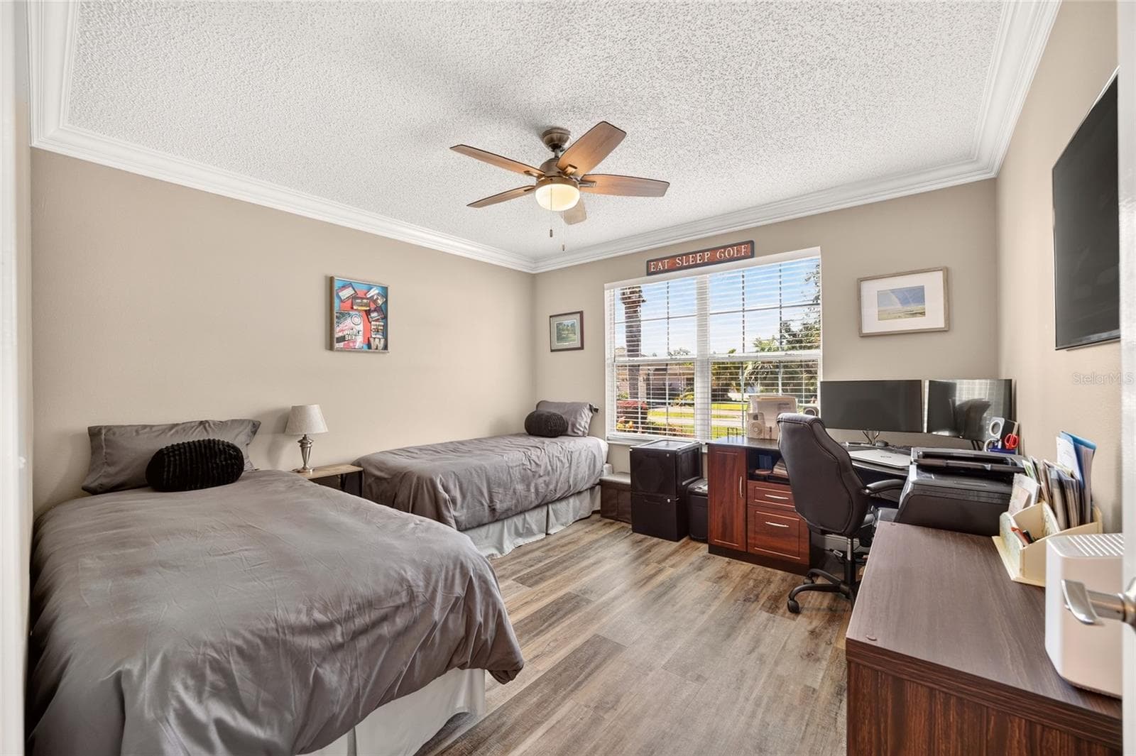 Guest Bedroom / Office: Flexible secondary bedroom offers wood-look flooring, a ceiling fan, a large window, and ample space for both sleeping and workspace arrangements. - 2749 BANYAN PL, THE VILLAGES