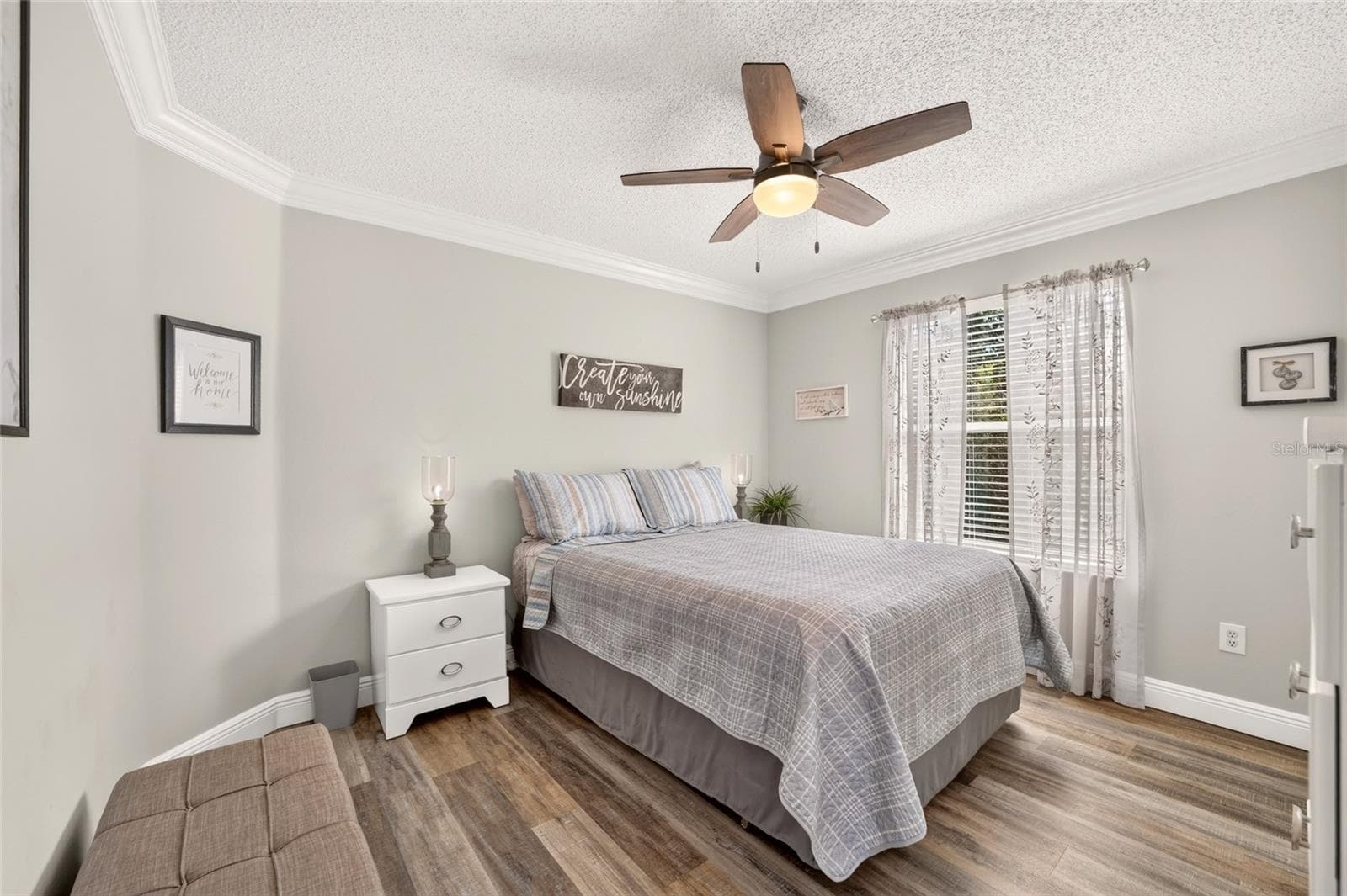 Guest Bedroom: Bright secondary bedroom includes wood-look flooring, crown molding, a ceiling fan, and a large window for natural light. - 2749 BANYAN PL, THE VILLAGES