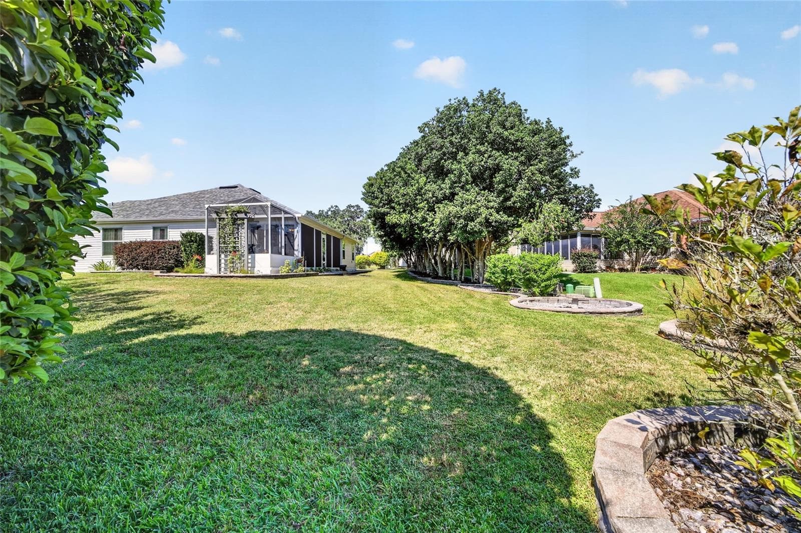 Backyard: Expansive lawn is framed by mature landscaping and established trees, with the screened outdoor living areas visible from the yard. - 2749 BANYAN PL, THE VILLAGES