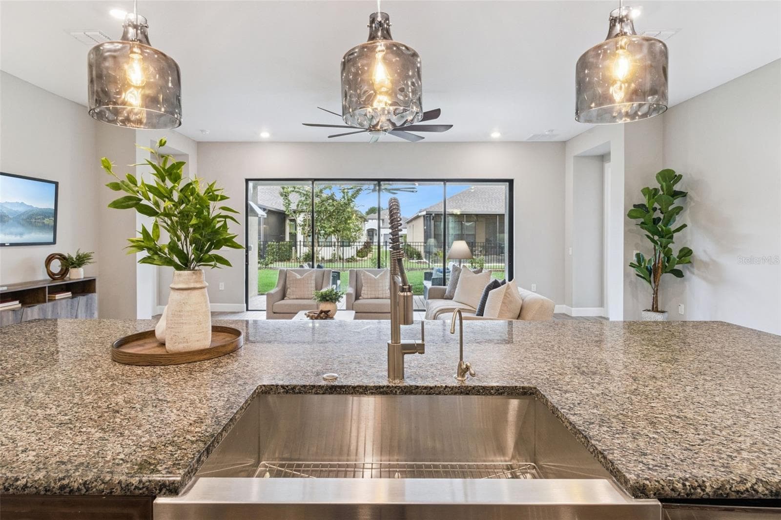 View from the kitchen sink across granite counters to the living area and covered patio. - 4108 VIA TOLEDO CT, POINCIANA