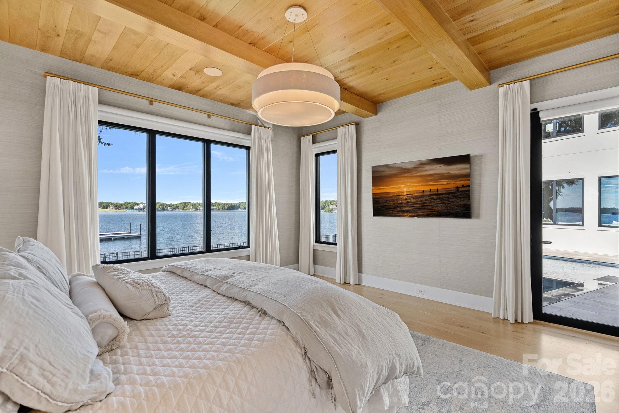 Serene waterfront primary suite framed by sweeping lake views, a warm wood-plank ceiling with exposed beams and direct access to the pool terrace. - 17811 Largo Place, Cornelius