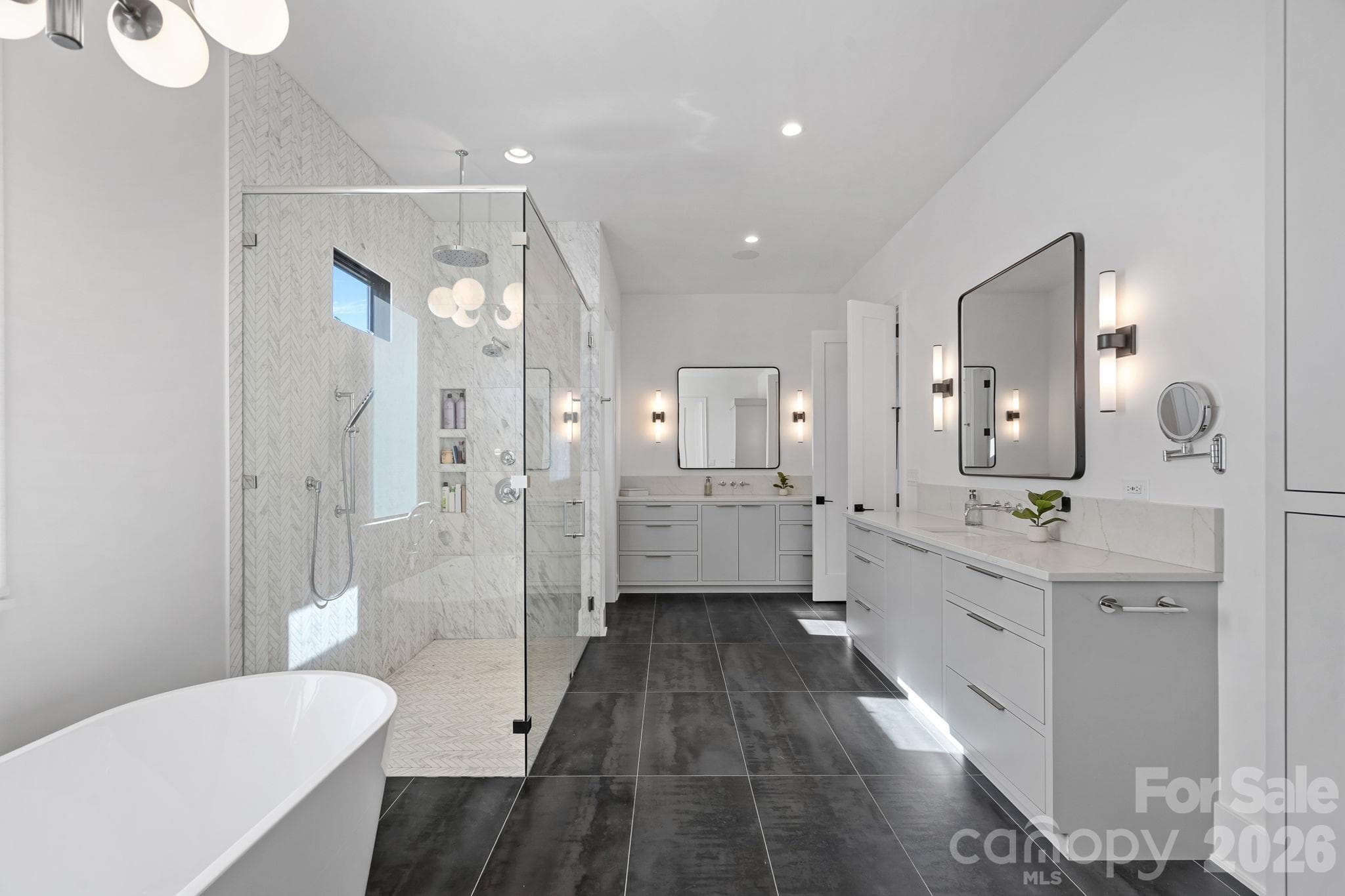 Spa-inspired primary ensuite with dual vanities, a freestanding soaking tub and an oversized glass-enclosed shower with multiple shower fixtures and designer tilework. - 17811 Largo Place, Cornelius