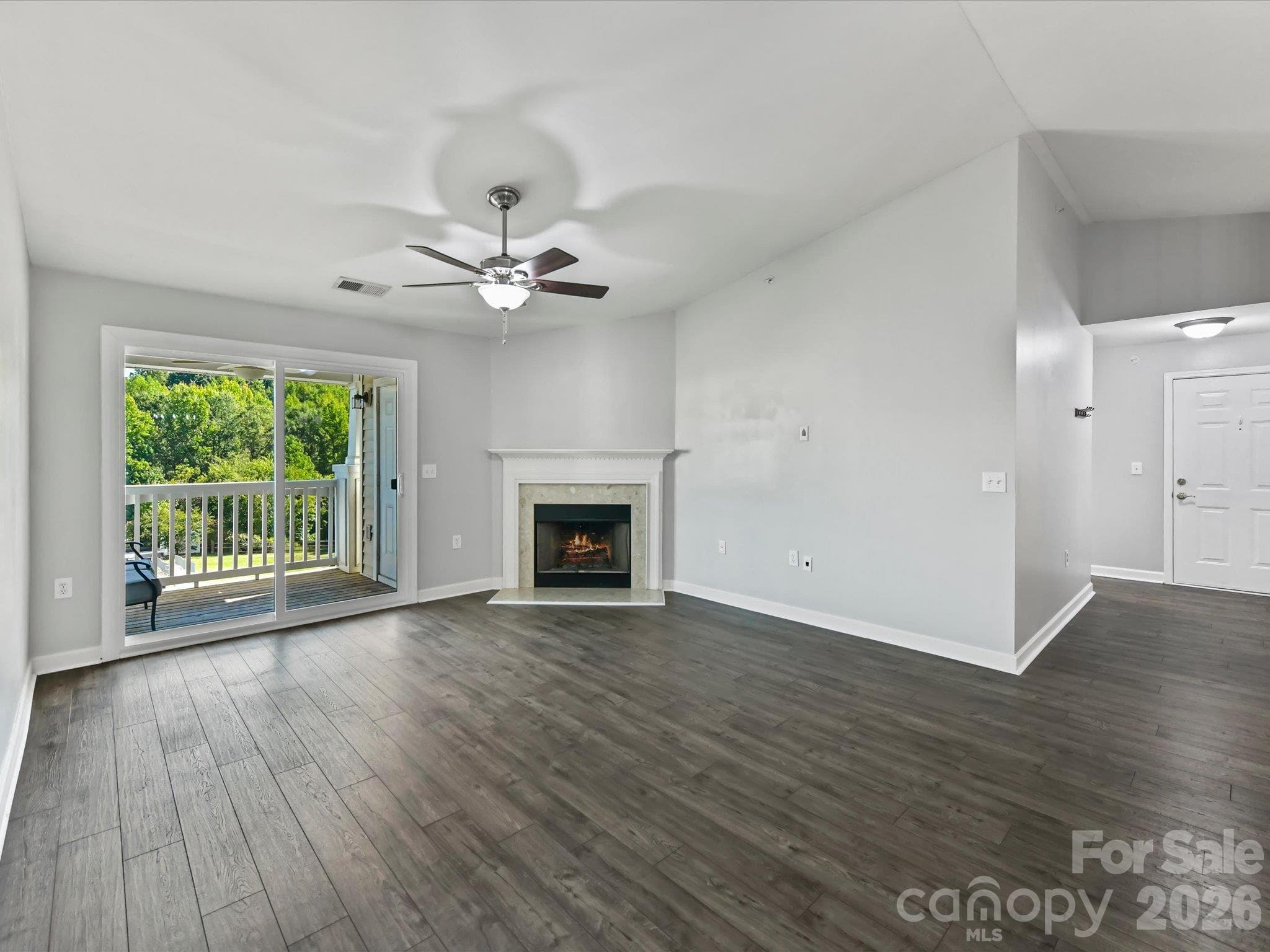 Spacious living room featuring durable LVP flooring, a cozy fireplace, ceiling fan, and sliding glass doors providing abundant natural light and direct access to the covered balcony. - 9031 Mcdowell Creek Court, Cornelius