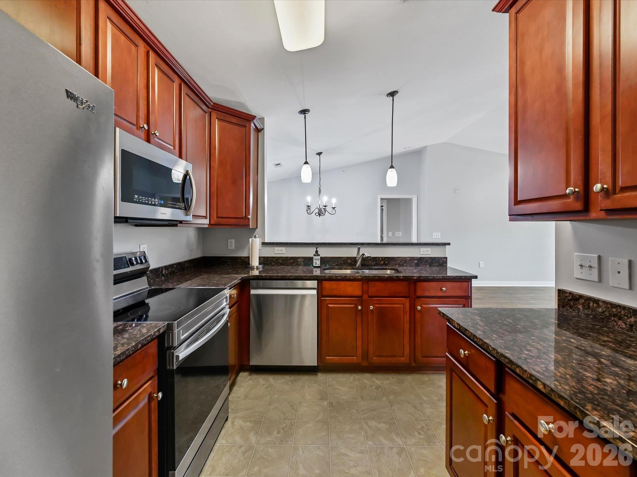 Well-appointed kitchen featuring rich wood cabinetry, granite countertops, stainless steel appliances, ample storage, and a convenient breakfast bar overlooking the adjoining living and dining areas. - 9031 Mcdowell Creek Court, Cornelius