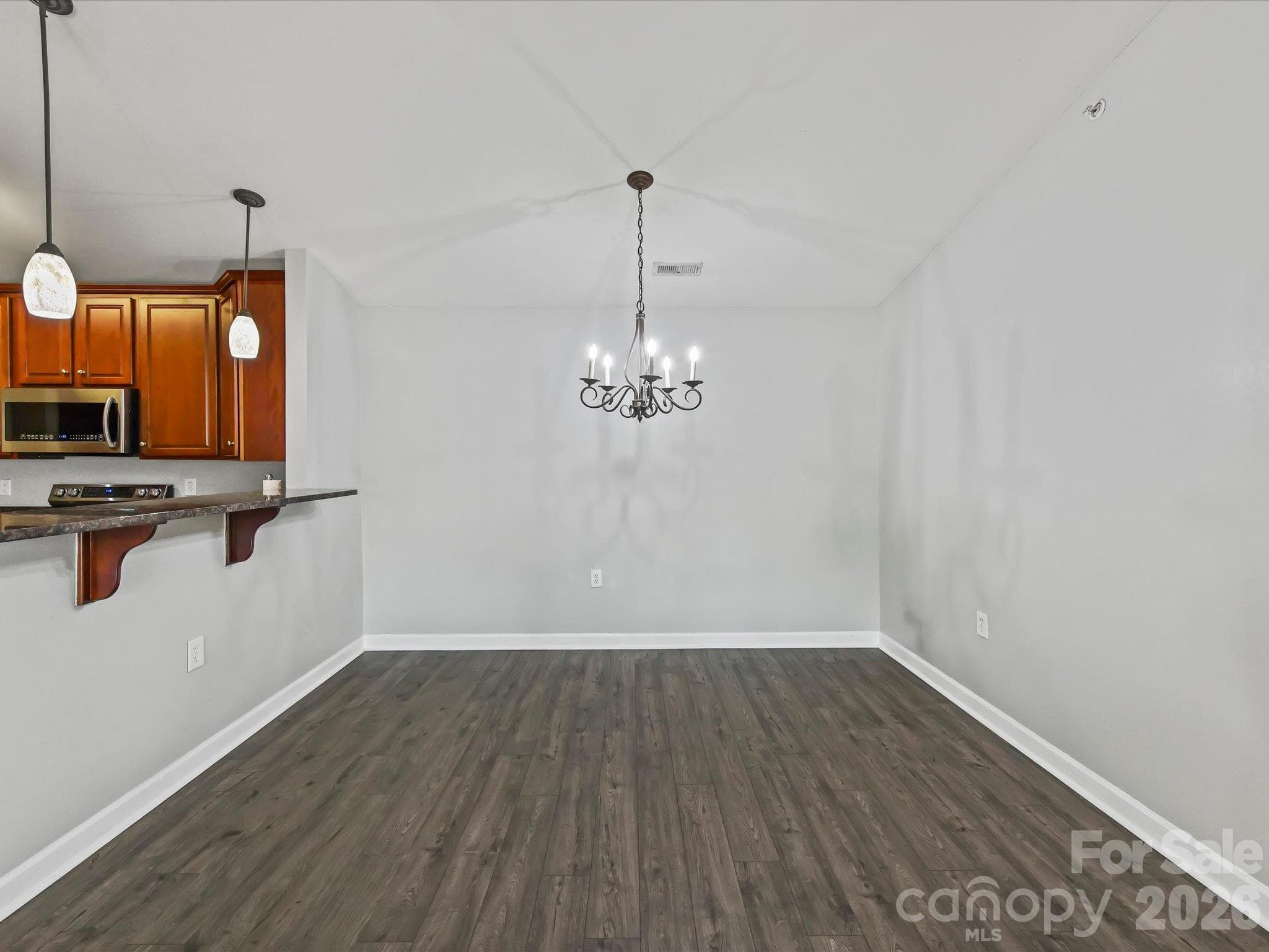 Spacious dining area featuring LVP flooring, a vaulted ceiling, decorative chandelier, and a convenient breakfast bar connecting seamlessly to the kitchen. - 9031 Mcdowell Creek Court, Cornelius