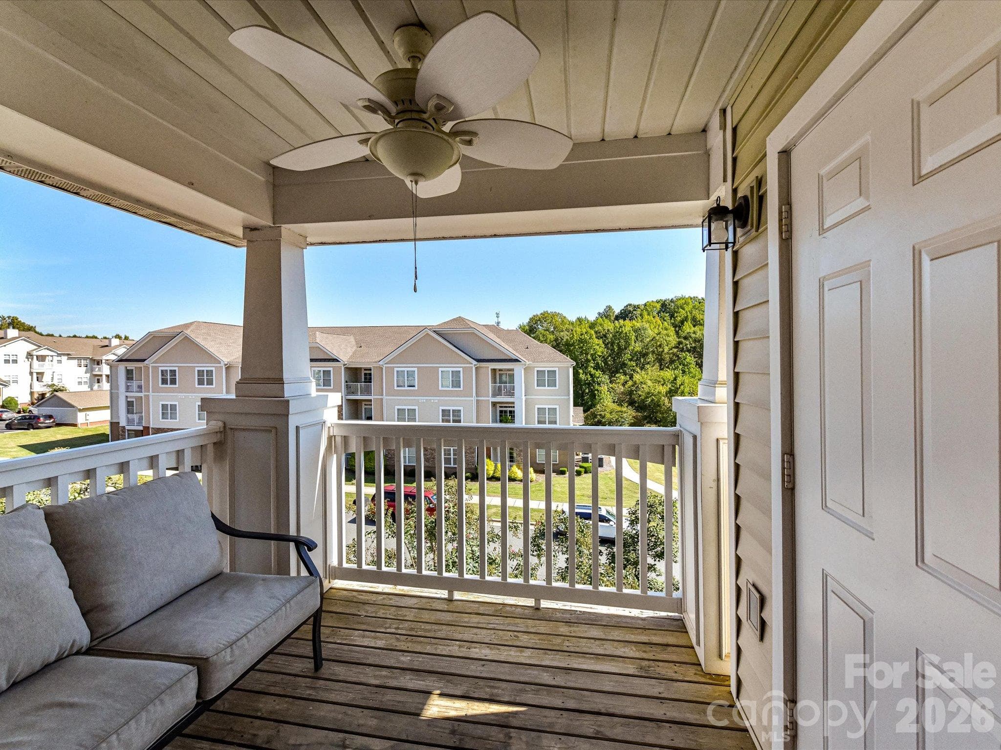 Covered balcony featuring a ceiling fan, outdoor seating, and an elevated view overlooking the surrounding community and mature greenery. - 9031 Mcdowell Creek Court, Cornelius