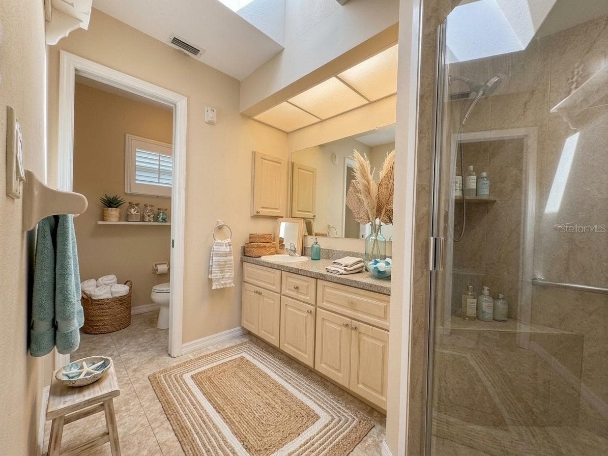 Primary Bathroom | Primary bathroom featuring a skylight for natural light, stone tiled shower, and vanity with storage. - 23088 GRAY AVE, PORT CHARLOTTE