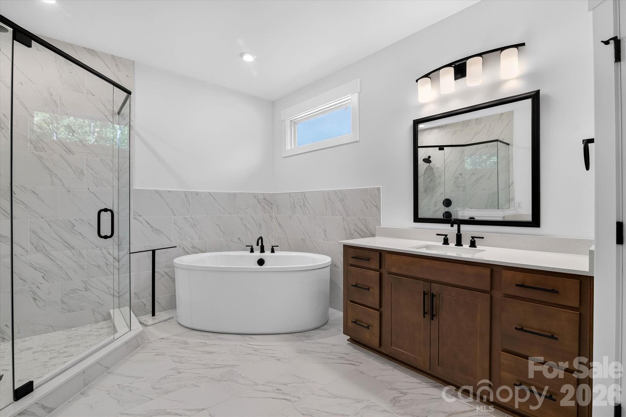 The freestanding tub isn't a feature, it's a standing invitation to end every single day well. Marble underfoot, black fixtures, and a glass shower make this feel more spa than en suite. - 1216 Glade Arch Lane, Huntersville