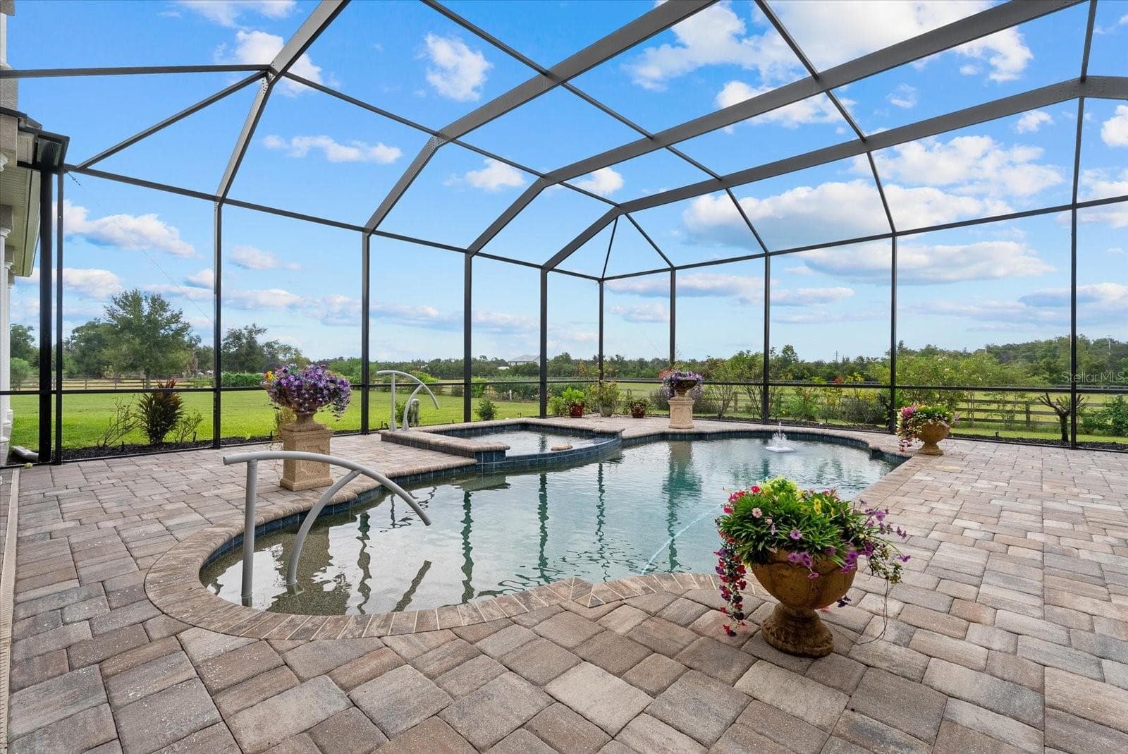 The pool deck is covered in brick paver, bronze colored pool screen and views of the back pastures - 520 RYE RD NE, BRADENTON