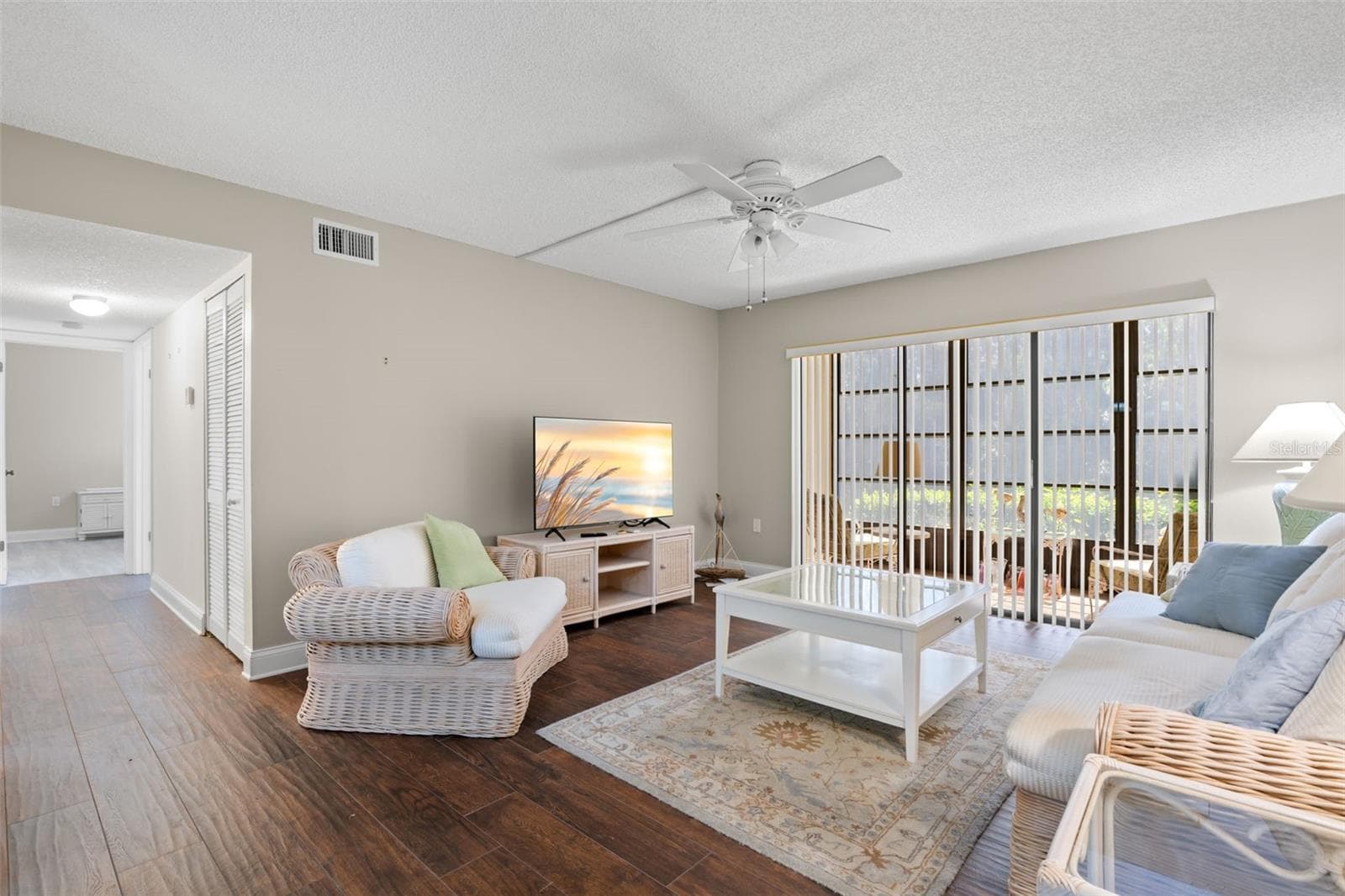 The living room features 2021 wood-look tile flooring, a ceiling fan, and wide sliding glass doors that open to the screened lanai and preserve view beyond. - 3188 LAKE PINE WAY S #F1, TARPON SPRINGS