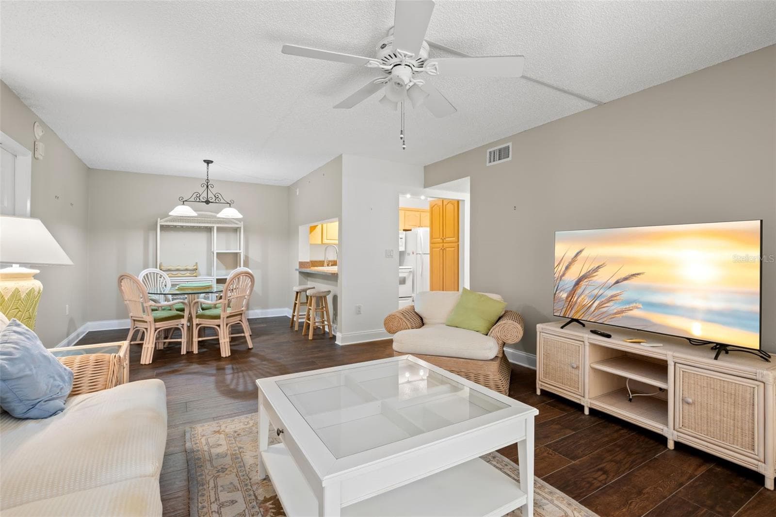 Neutral tones, a ceiling fan, and 2021 wood-look tile flooring carry through the open living and dining areas, with a pass-through connecting the kitchen to the main living space. - 3188 LAKE PINE WAY S #F1, TARPON SPRINGS
