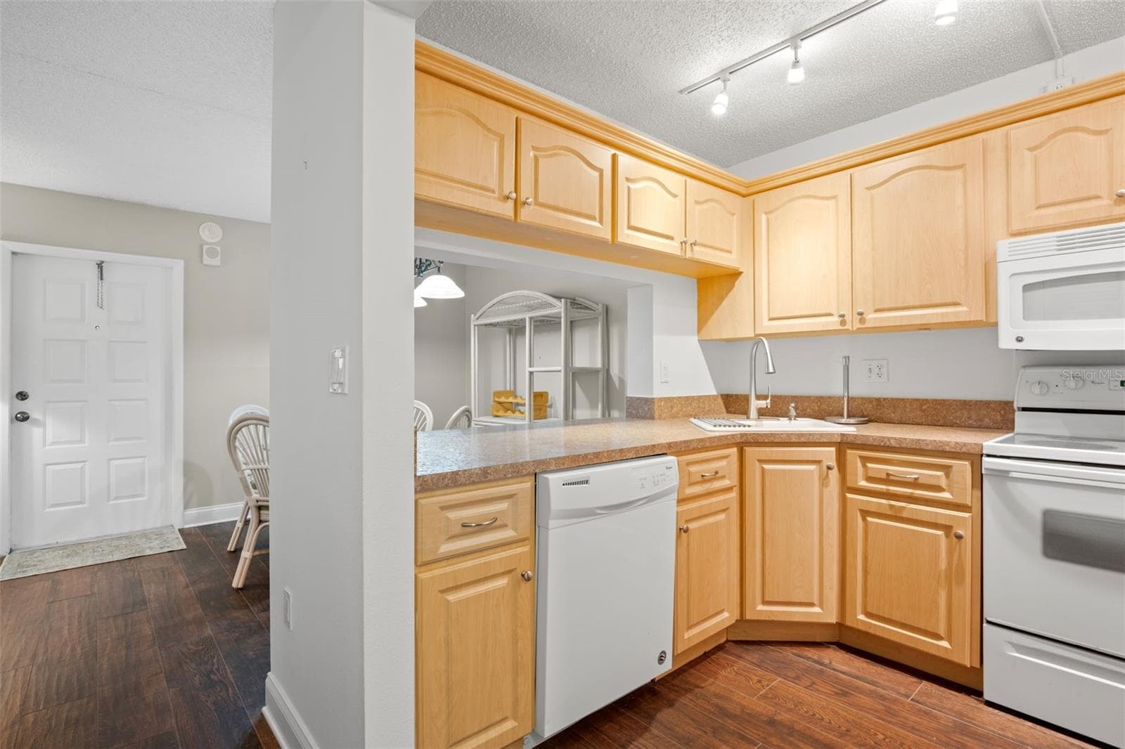 The kitchen wraps around the corner with plentiful cabinetry and counter space, a corner sink, track lighting, and an open pass-through that keeps it connected to the dining area. - 3188 LAKE PINE WAY S #F1, TARPON SPRINGS