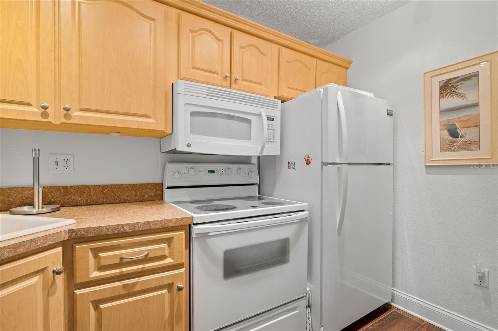 White appliances keep the kitchen bright and cohesive, with an electric range, built-in microwave, and full-size refrigerator framed by abundant upper cabinetry. - 3188 LAKE PINE WAY S #F1, TARPON SPRINGS