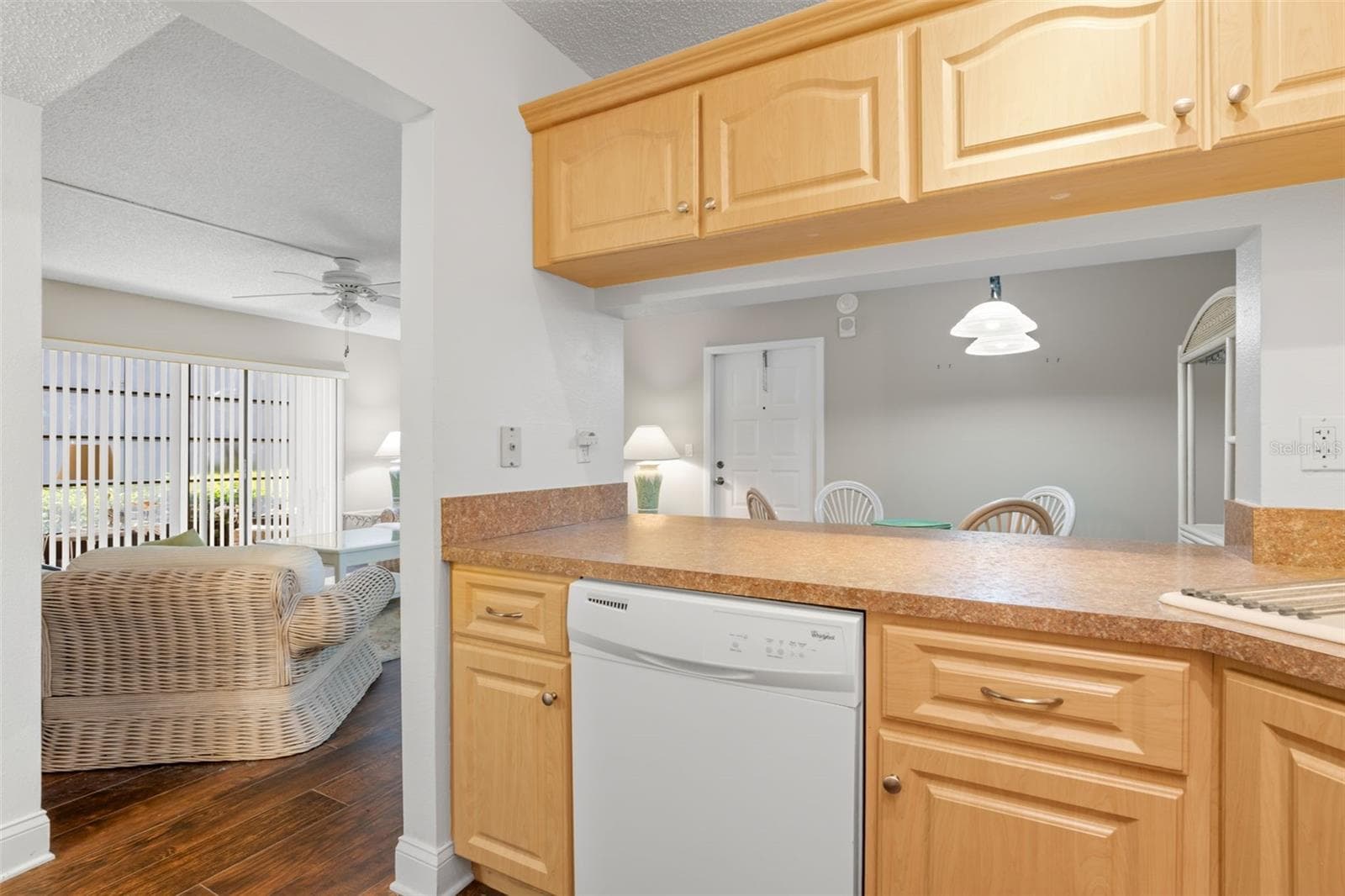 The kitchen’s wide pass-through doubles as a breakfast bar, with warm wood cabinetry, generous counter space, and a dishwasher positioned conveniently beneath. - 3188 LAKE PINE WAY S #F1, TARPON SPRINGS
