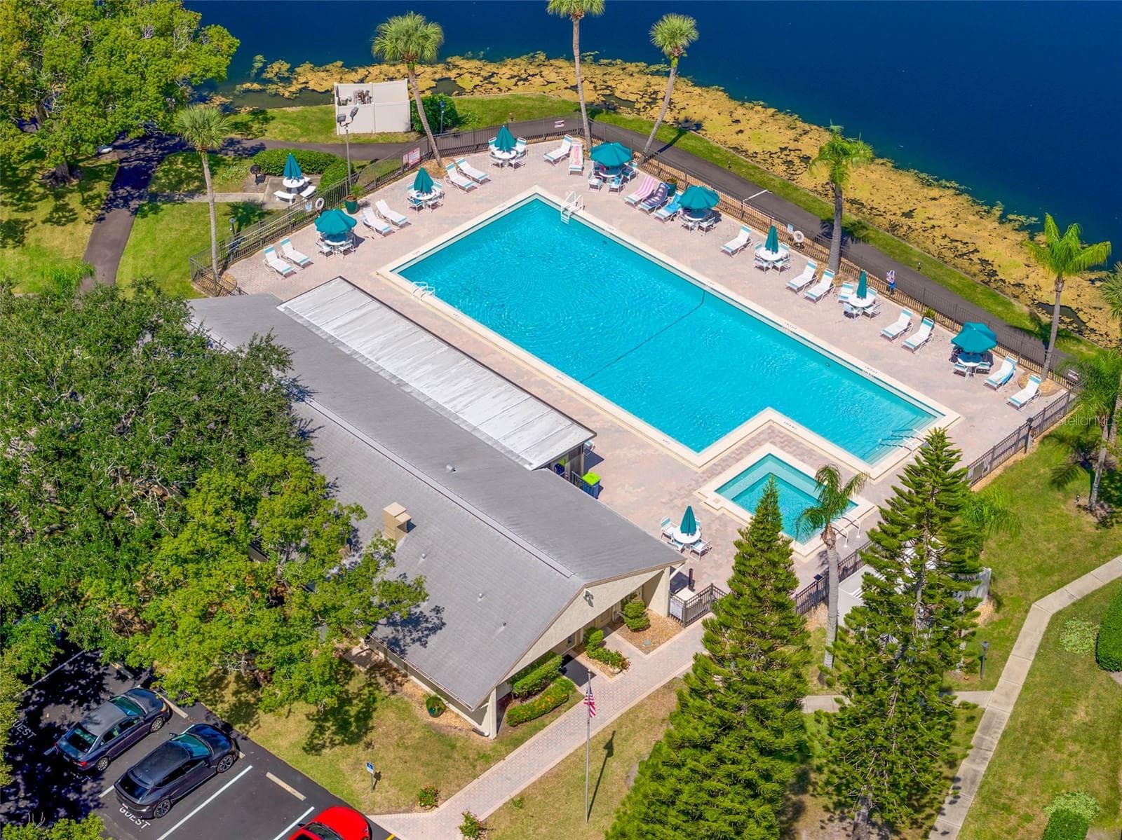 A pristine lakeside pool anchors the community’s recreation area, surrounded by palm trees, lounge seating, and a separate spa—an inviting place to swim, unwind, and enjoy the Florida sunshine. - 3188 LAKE PINE WAY S #F1, TARPON SPRINGS