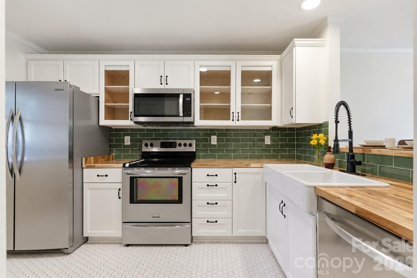New recessed lighting highlights the kitchen’s fresh finishes, while a farmhouse sink, green tile backsplash, and glass-front cabinetry blend modern style with timeless charm. - 3858 Mosscroft Lane, Charlotte