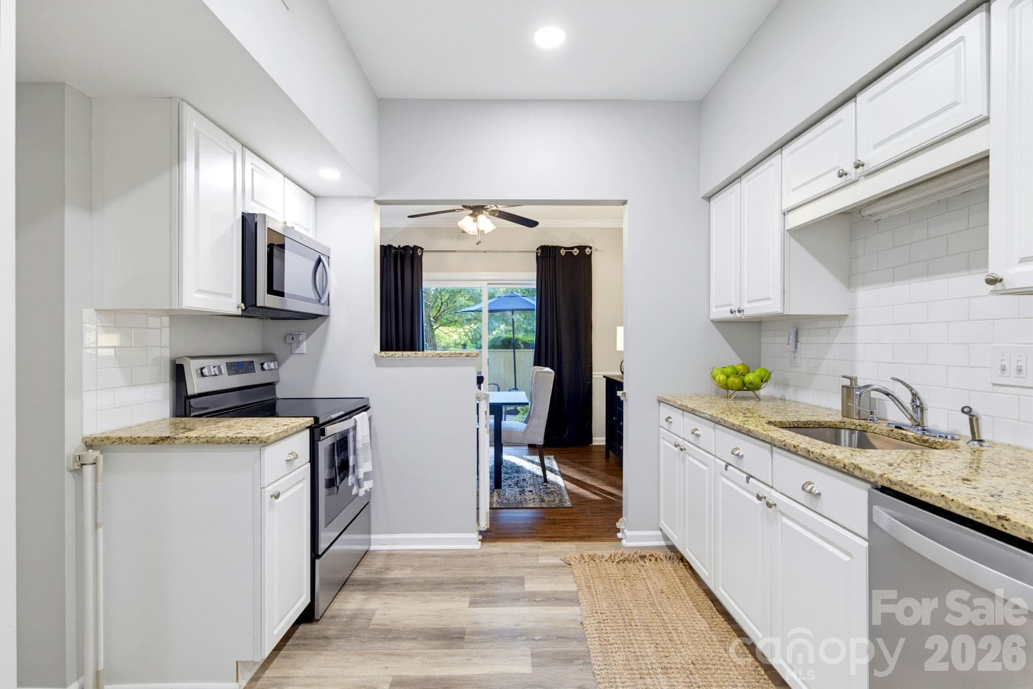 Bright galley-style kitchen with white cabinetry, granite countertops and an easy flow into the adjoining dining area - 5901 Quail Hollow Road, Charlotte
