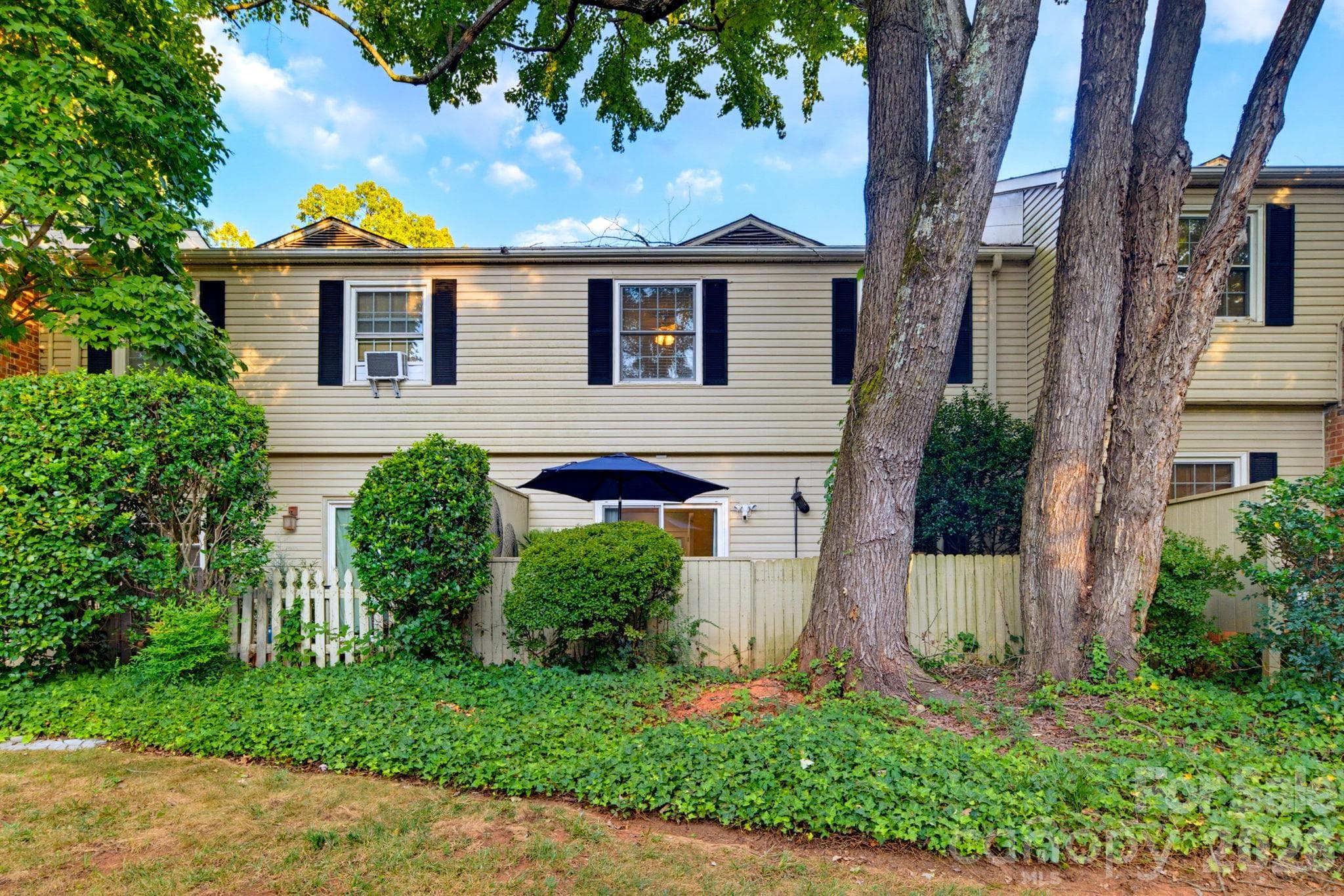 Rear exterior view showing the enclosed patio and mature trees and landscaping - 5901 Quail Hollow Road, Charlotte