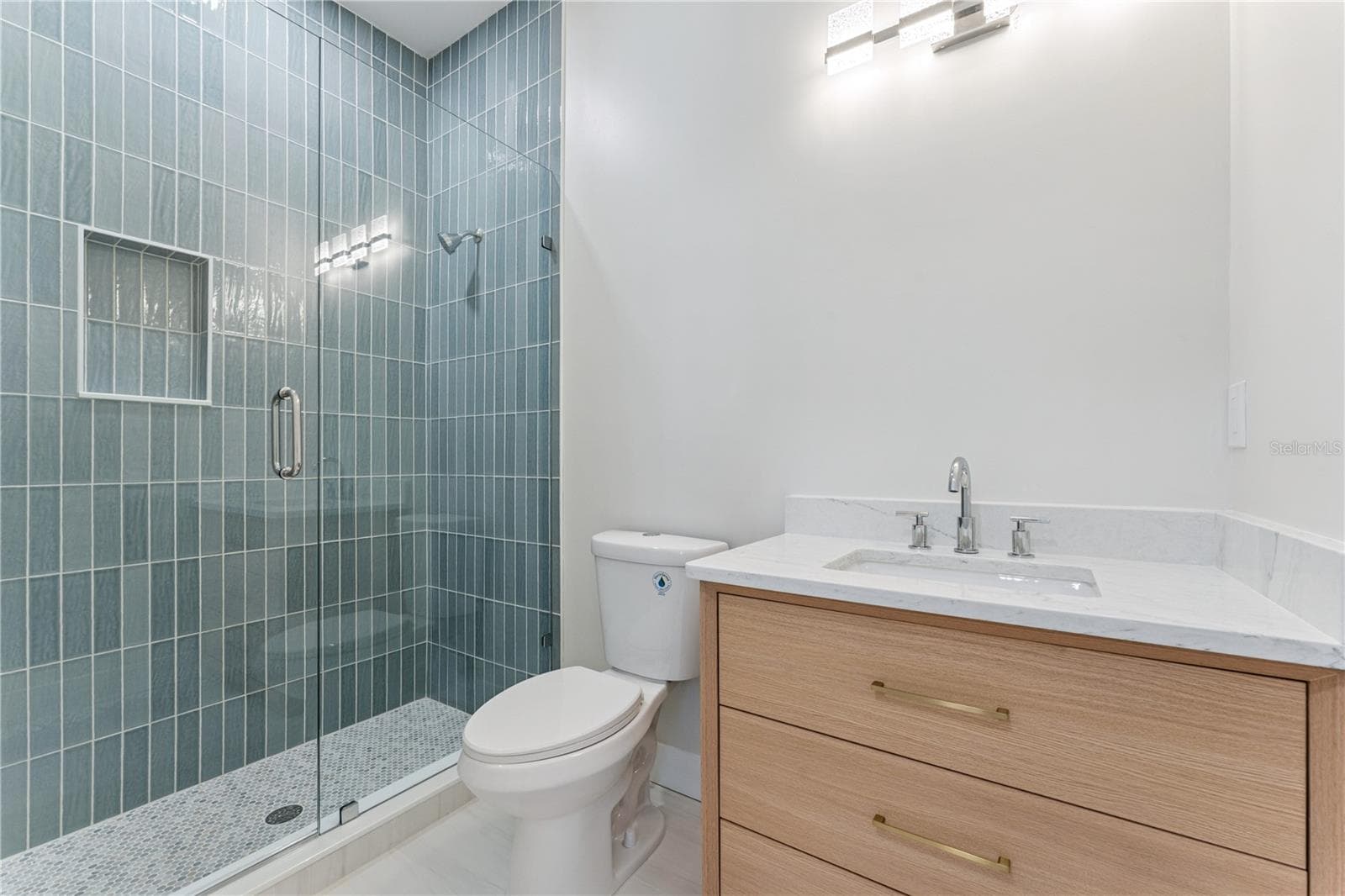 Blue shower tile and a wood-toned vanity add color and warmth to this bathroom. - 3456 FAIRWAY LN, ORLANDO