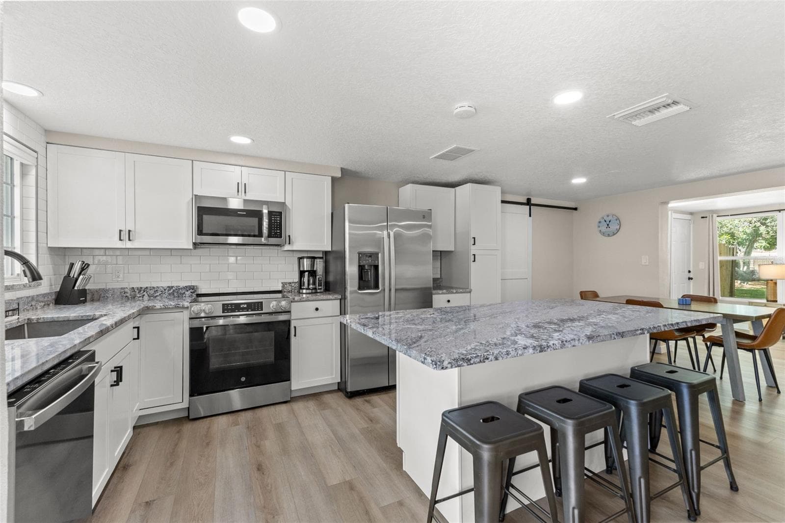Renovated kitchen with white cabinetry, granite countertops, stainless steel appliances, and an oversized island with seating for four. - 201 SOUTH ST, PALM HARBOR