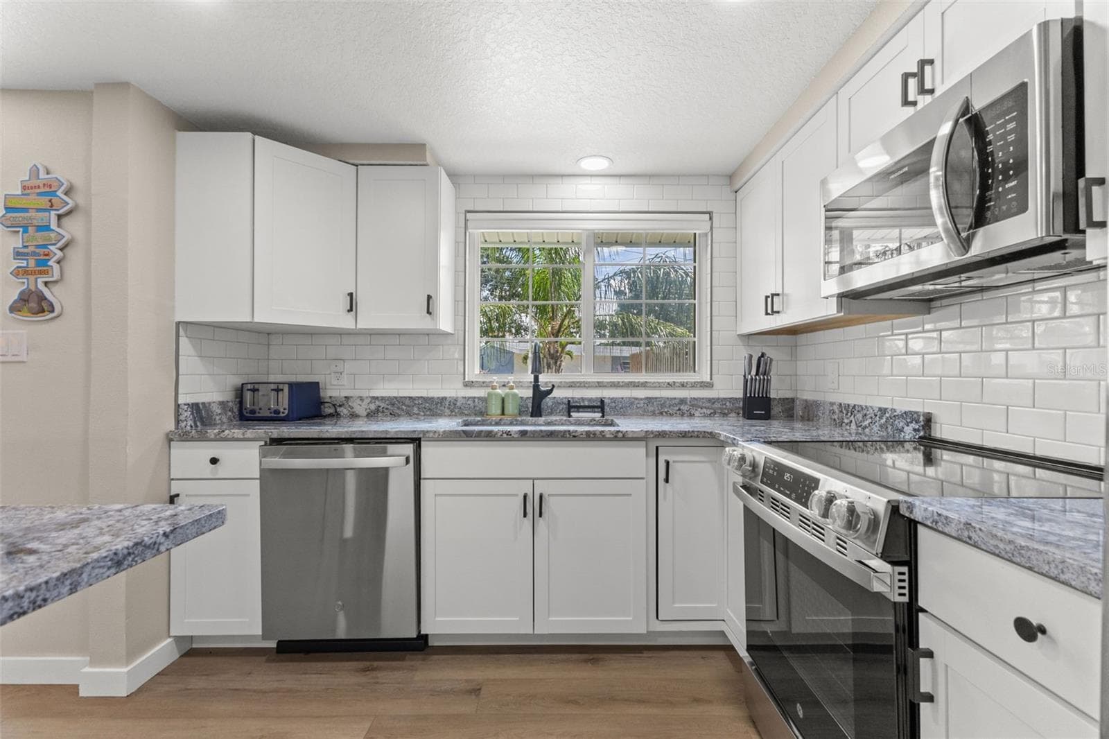 White cabinetry, granite countertops, subway tile backsplash, stainless steel appliances, and a window above the kitchen sink. - 201 SOUTH ST, PALM HARBOR