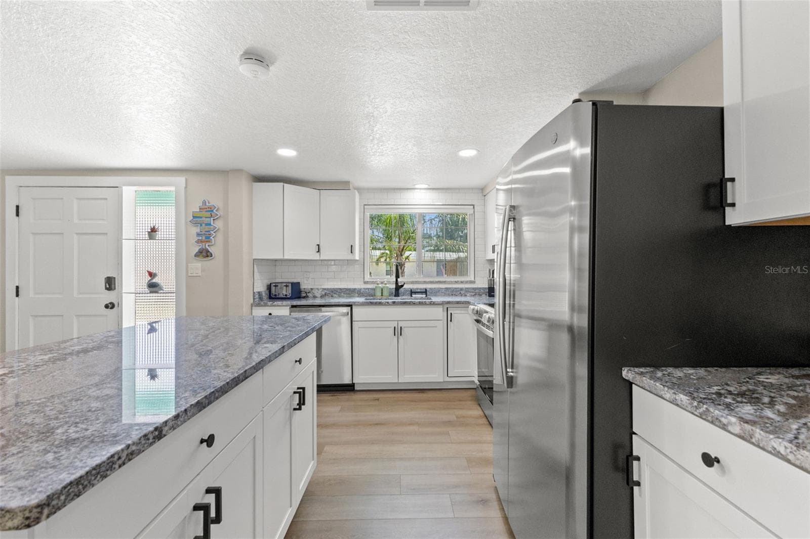 Another view highlights the kitchen’s extensive cabinetry, stainless steel appliances, granite surfaces, and luxury vinyl plank flooring. - 201 SOUTH ST, PALM HARBOR