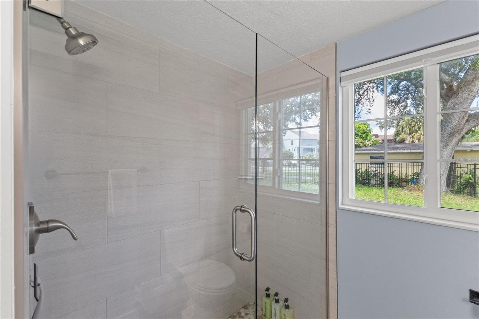 Updated bathroom features a glass-enclosed walk-in shower with large-format tile and pebble-style shower flooring. - 201 SOUTH ST, PALM HARBOR