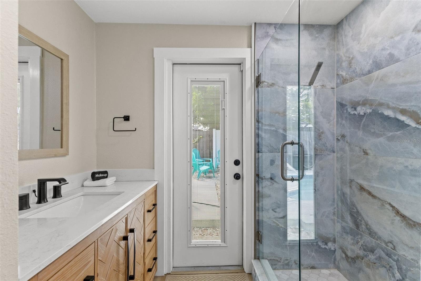 Updated bath features a modern vanity, quartz-style countertop, black fixtures, and a striking glass-enclosed tiled shower. - 201 SOUTH ST, PALM HARBOR