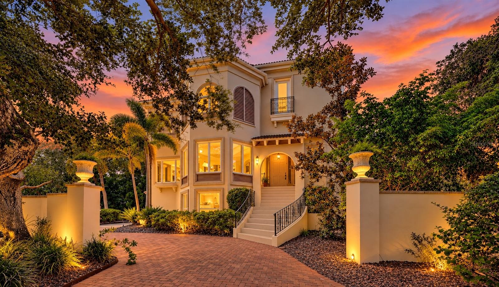 Warm architectural lighting and mature oaks create a striking sense of arrival as evening falls. - 168 COASTAL HAMMOCK CT, OSPREY