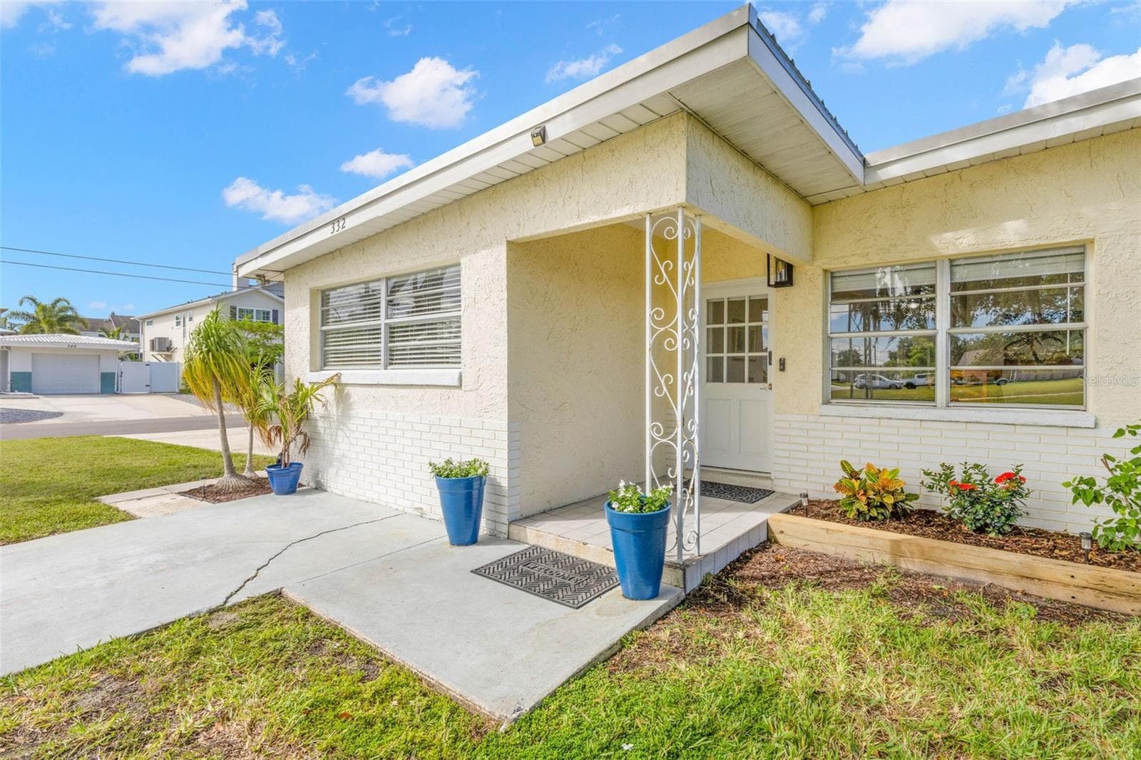 A covered front entry with classic decorative ironwork, bright planters, and a raised garden bed adds a cheerful welcome, while broad front windows bring plenty of natural light into the home. - 332 WESTWINDS DR, PALM HARBOR
