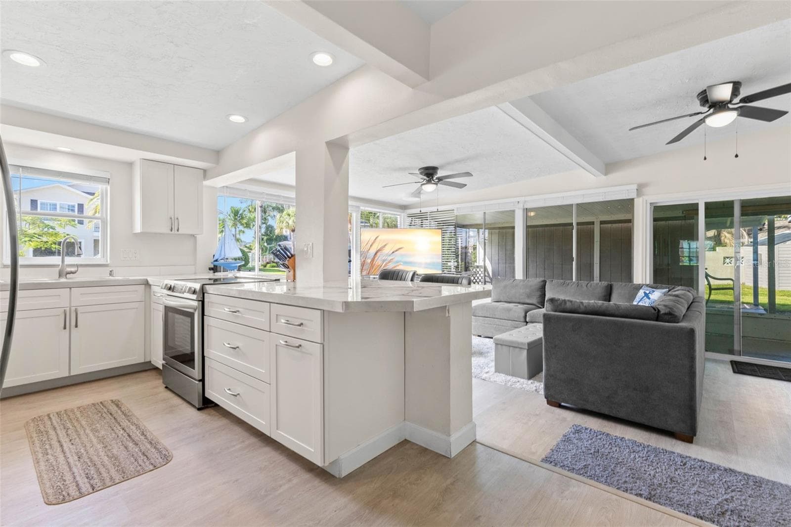 The updated kitchen (2025) opens directly to the living area and features crisp white cabinetry, stainless steel appliances, abundant counter space, recessed lighting, and a generous breakfast bar for casual seating or serving. - 332 WESTWINDS DR, PALM HARBOR