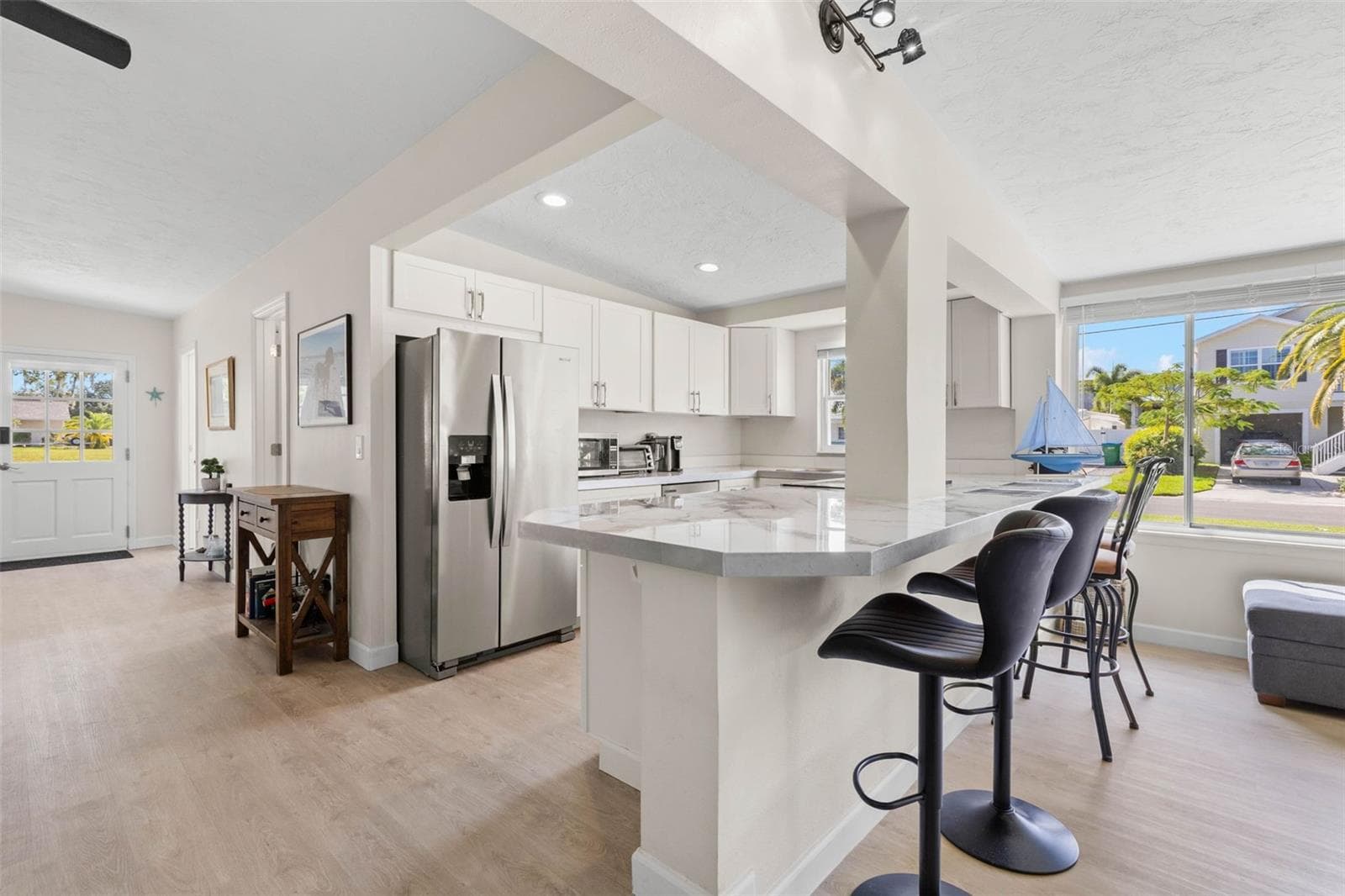 The updated kitchen (2025) pairs crisp white cabinetry and stainless steel appliances with expansive counter space and a wraparound breakfast bar that adds both seating and everyday functionality. - 332 WESTWINDS DR, PALM HARBOR