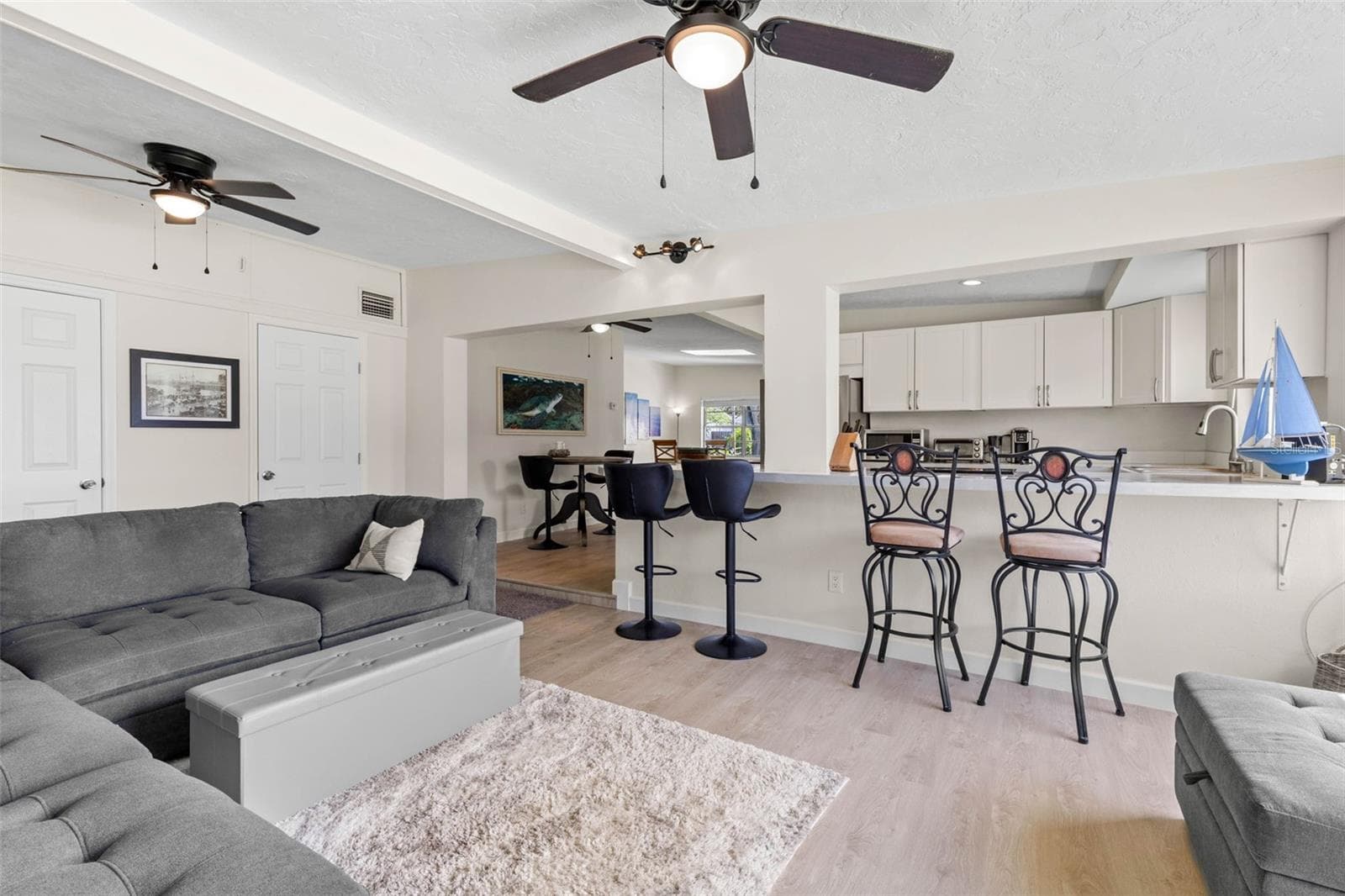 The spacious living area features dual ceiling fans, a soft neutral color palette, and 2025 luxury vinyl plank flooring, with an open connection to the kitchen and breakfast bar that keeps the space feeling relaxed, connected, and easy to use. - 332 WESTWINDS DR, PALM HARBOR